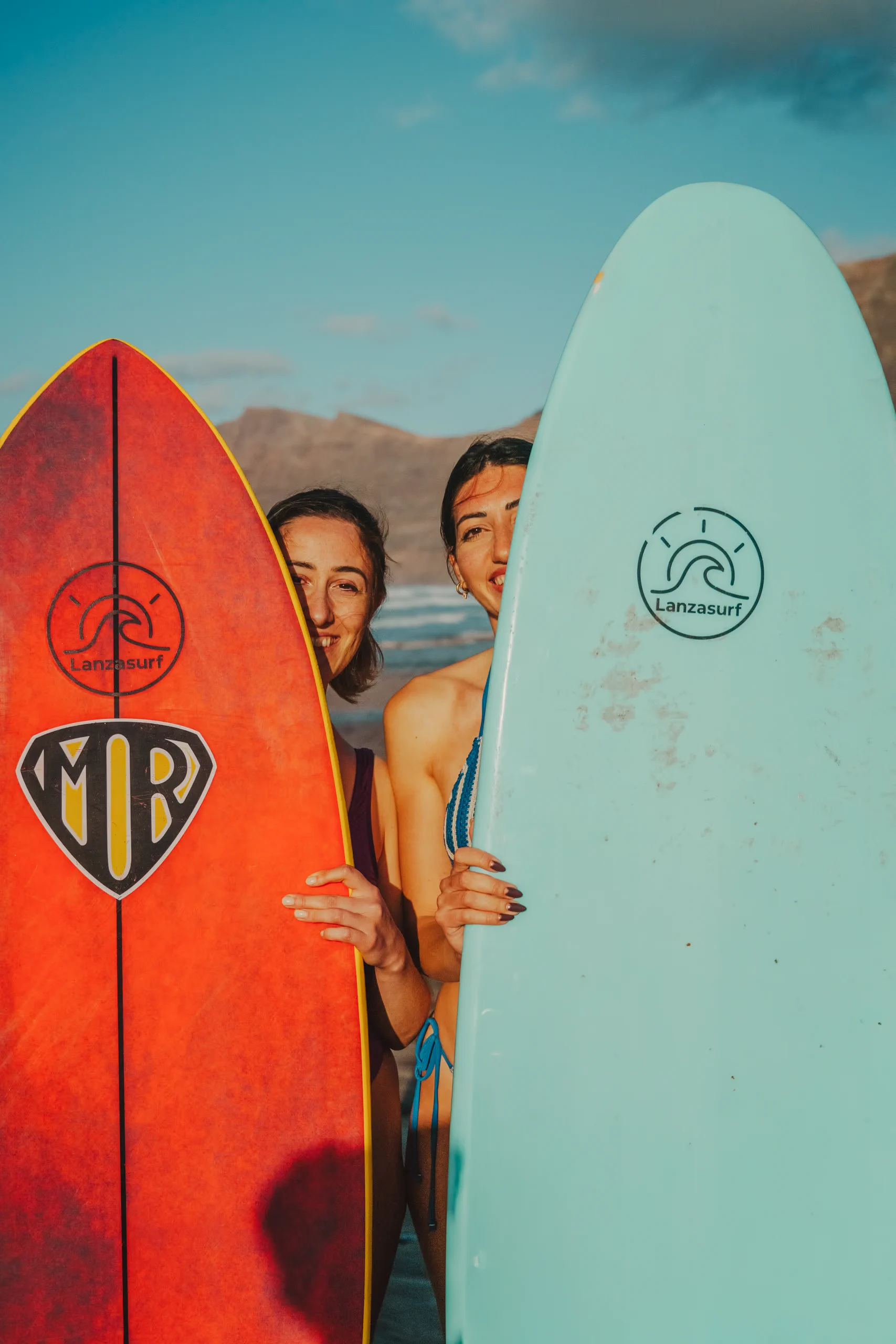 Letizia and Miriam behind two surfboard on the beach