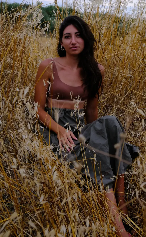 Miriam in piedi in un vasto campo di grano maturo illuminato dal sole nella campagna albanese.