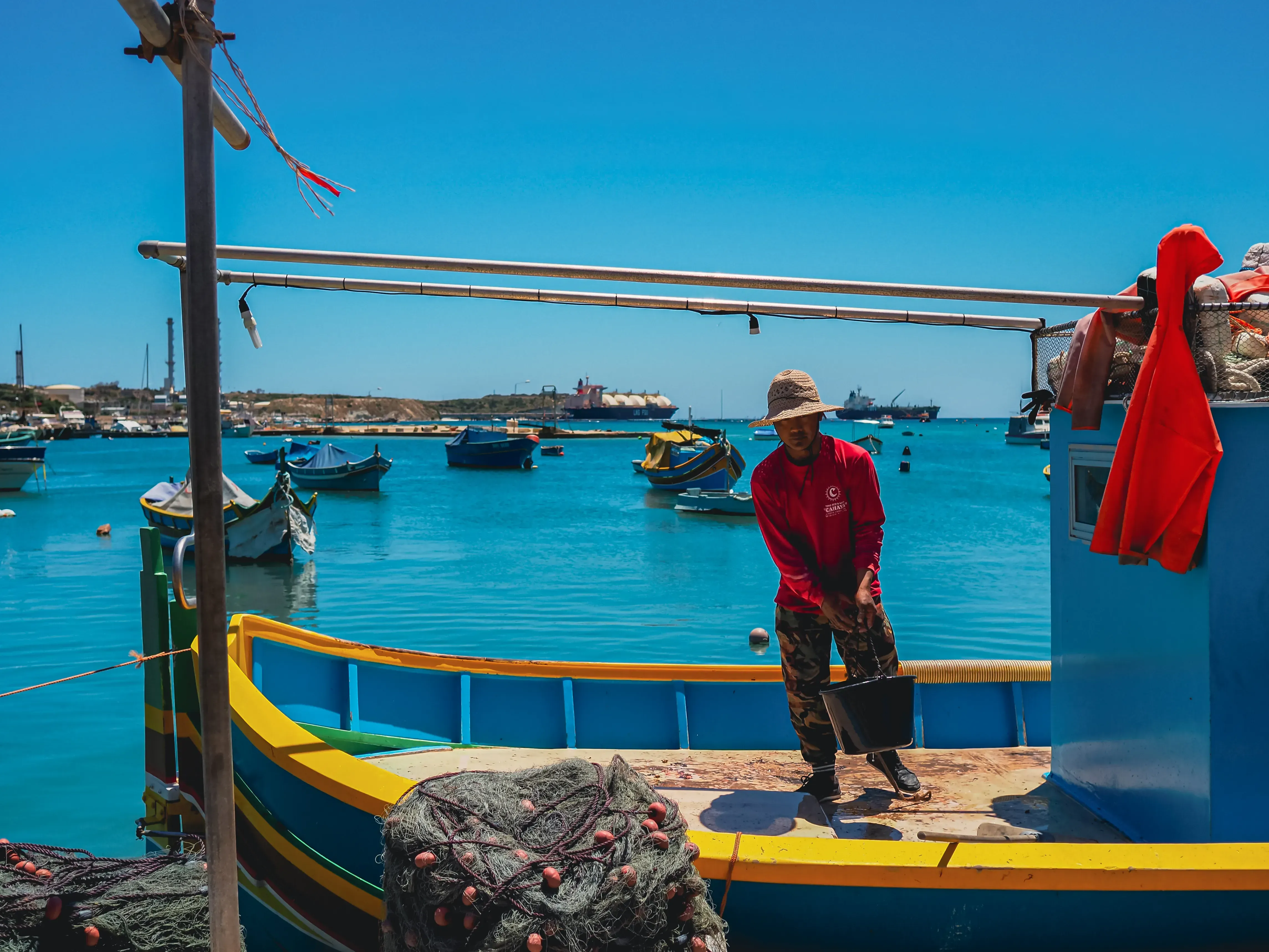 Local fisherman standing on a brightly colored Luzzu boats in the southern Maltese town.
