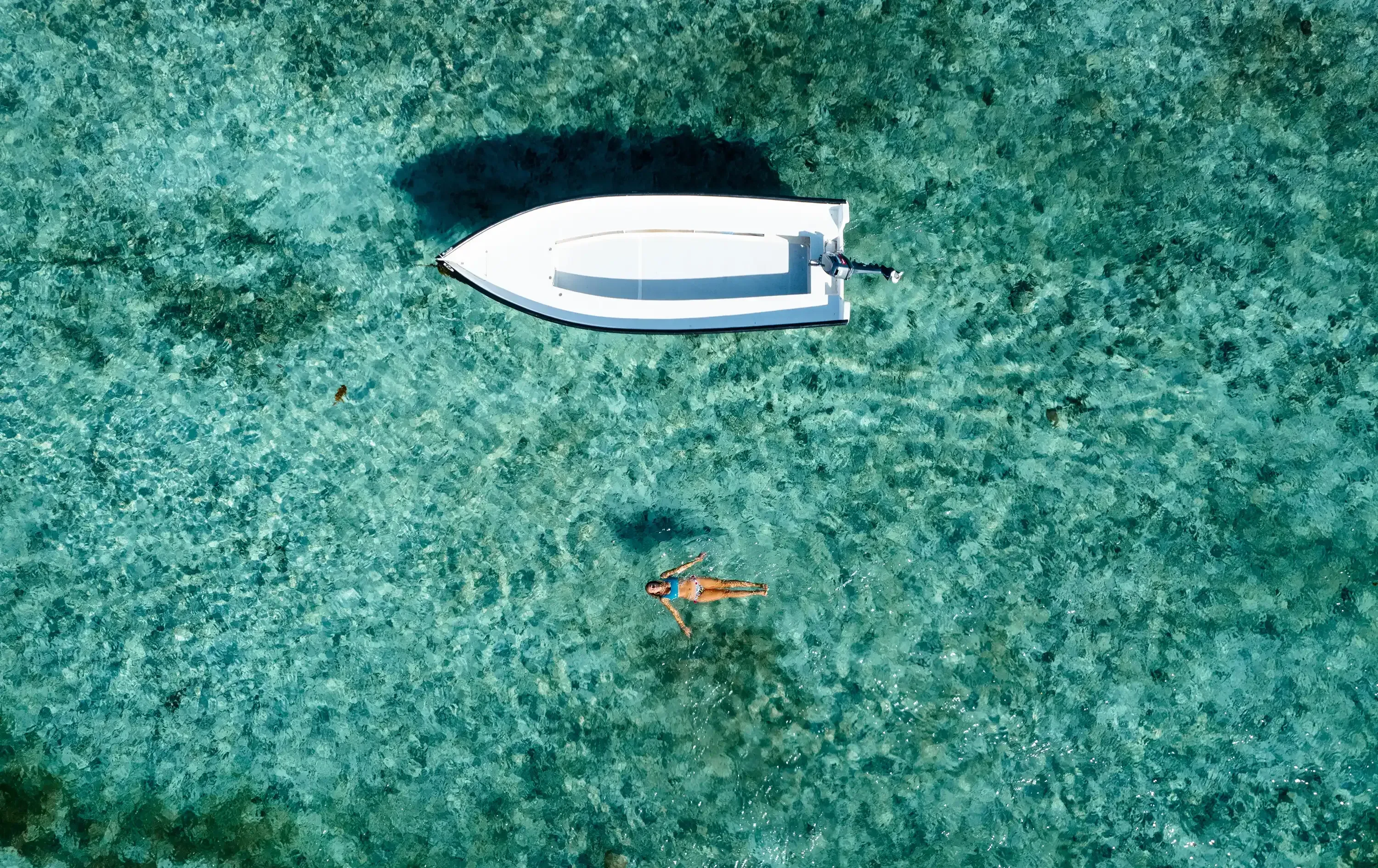 Drone shot showing Letizia and a small boat near the turquoise waters of Le Morne beach, with the iconic Le Morne Brabant mountain in the background.
