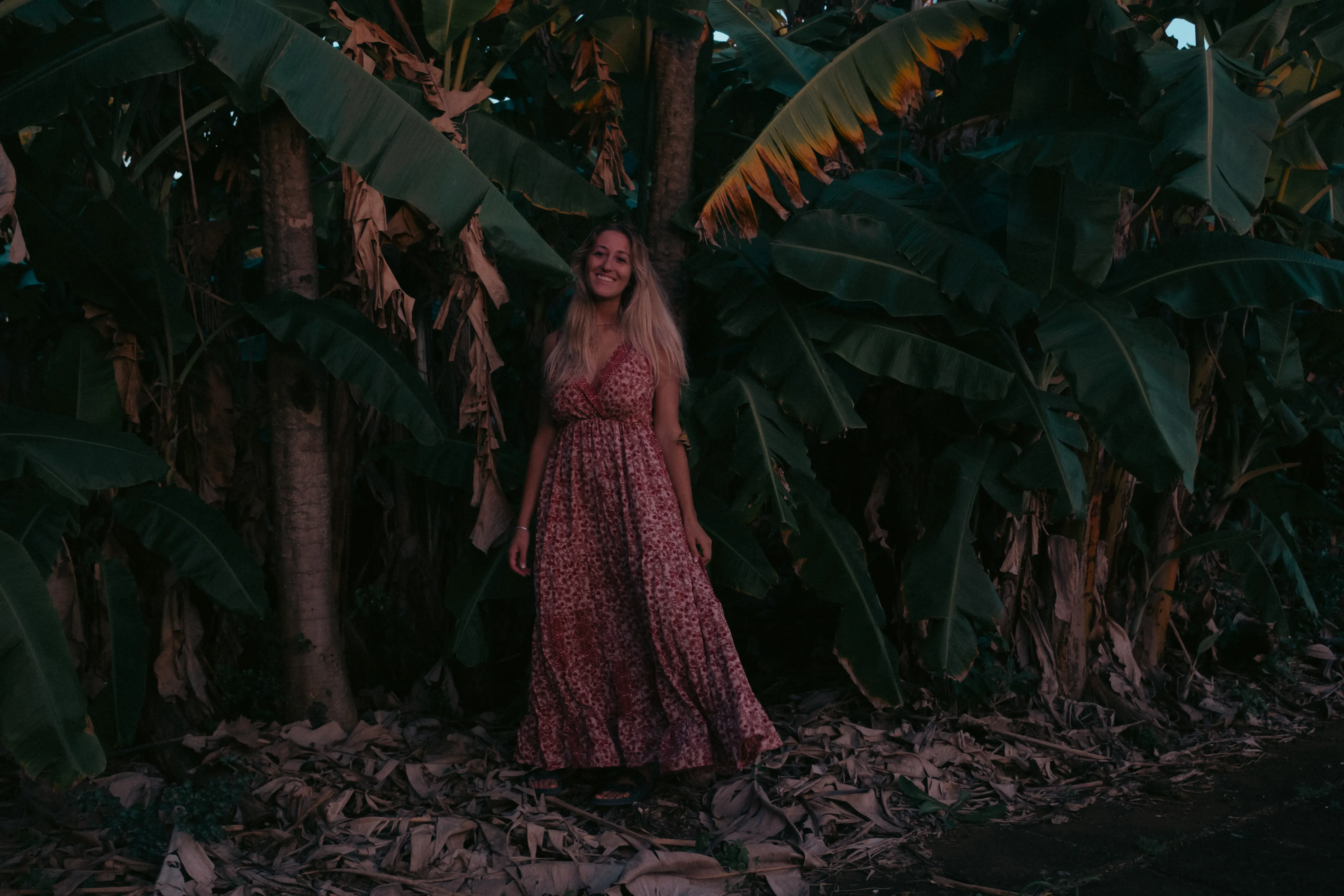 Letizia smiling amongst the large, green fronds and leaves of banana plants.