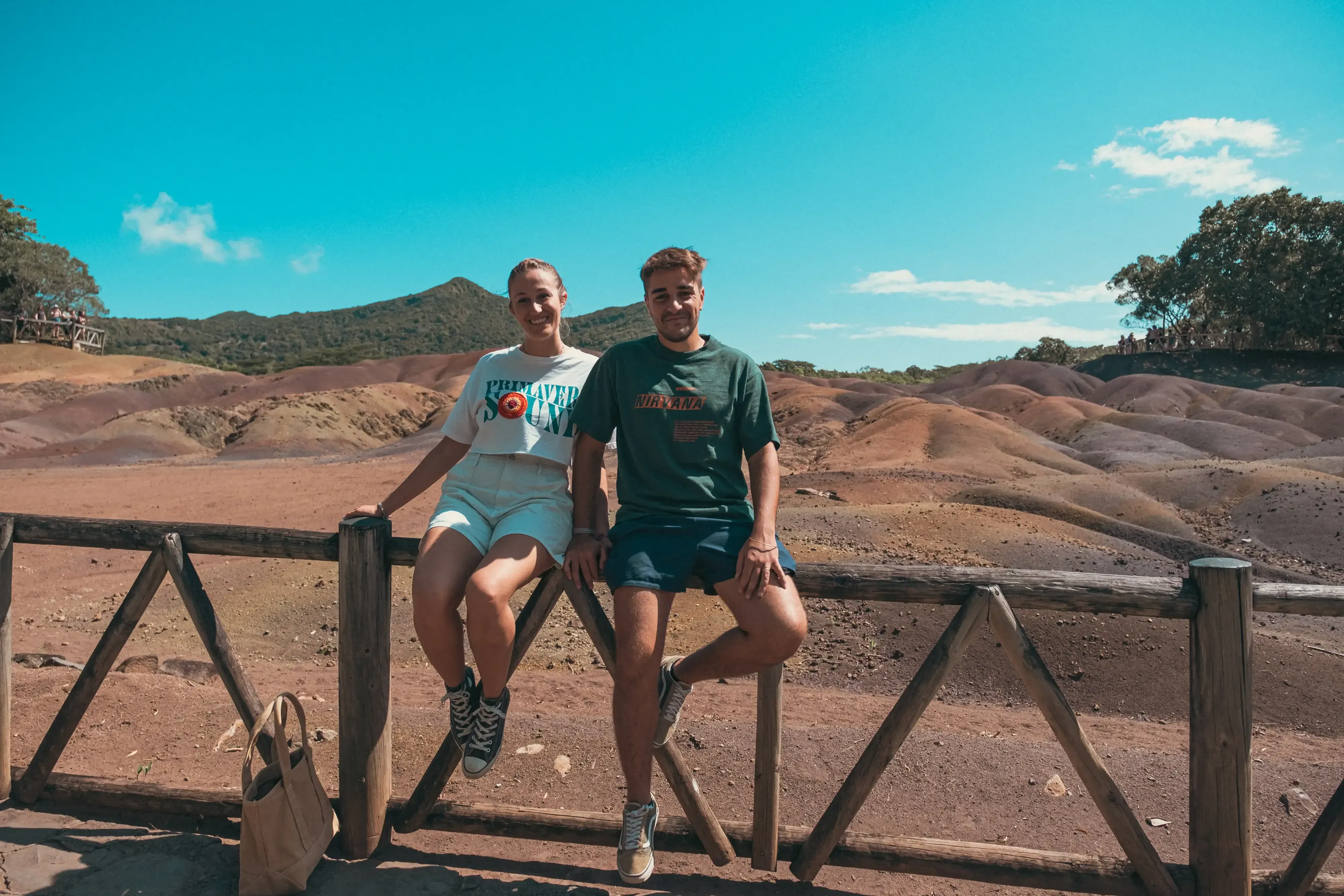 Letizia and Ieser sitting on the wooden fence or railing overlooking the Seven Coloured Earths natural phenomenon.