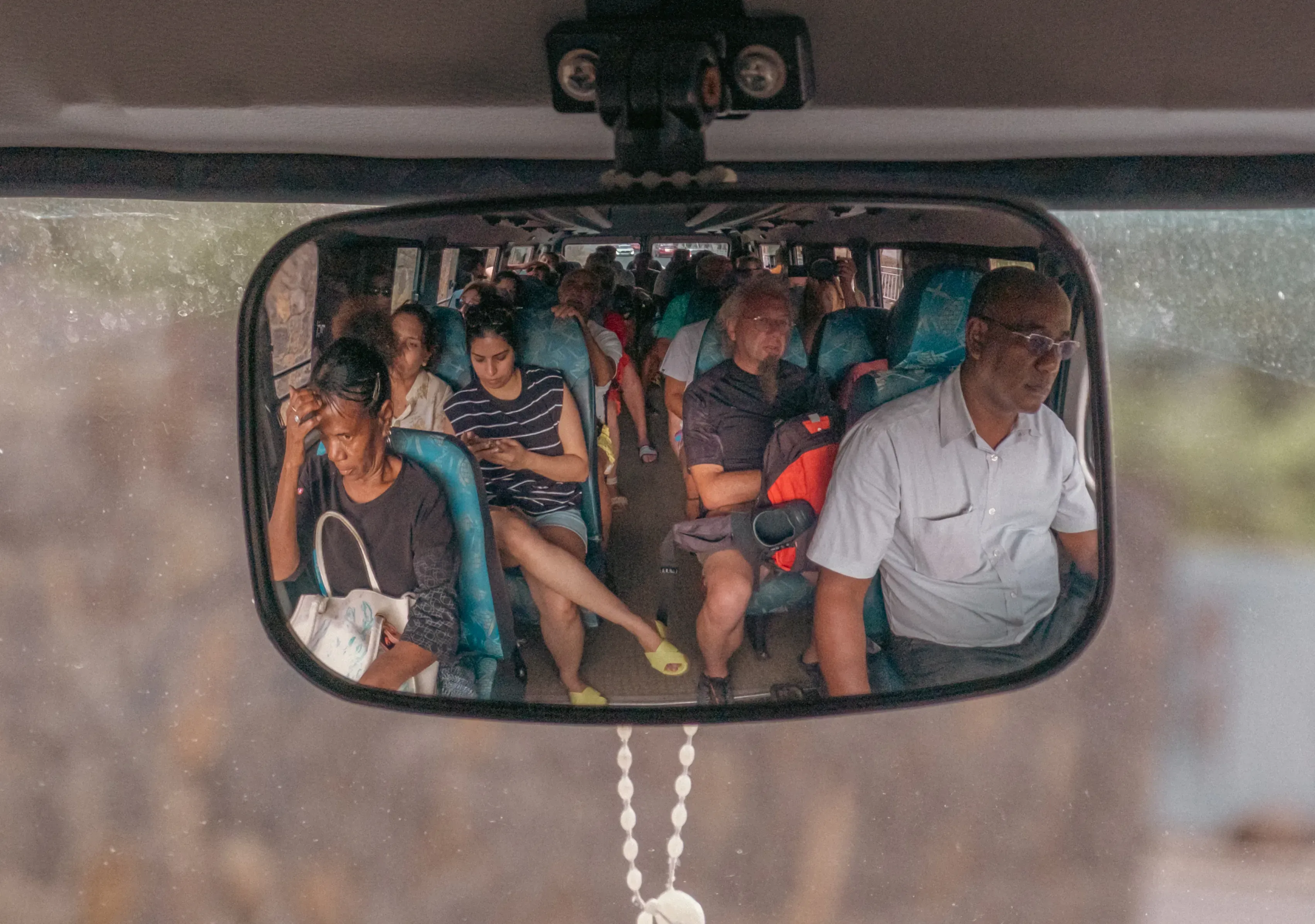 A candid photo taken inside a Mauritian bus, showing the view through the rearview mirror reflecting the road or passengers.