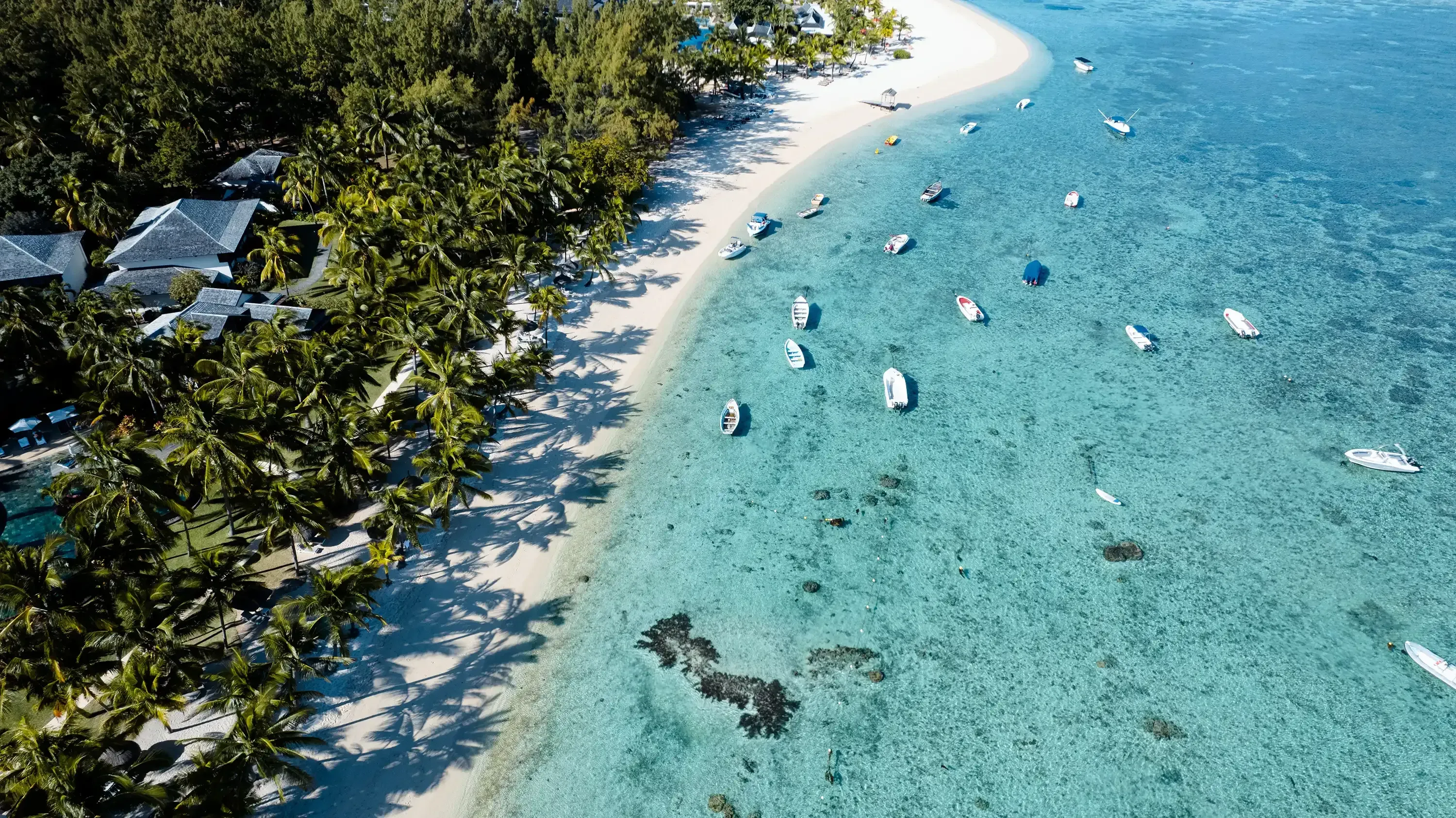 Aerial drone view of Le Morne beach, showing small boats anchored on the turquoise blue lagoon water.