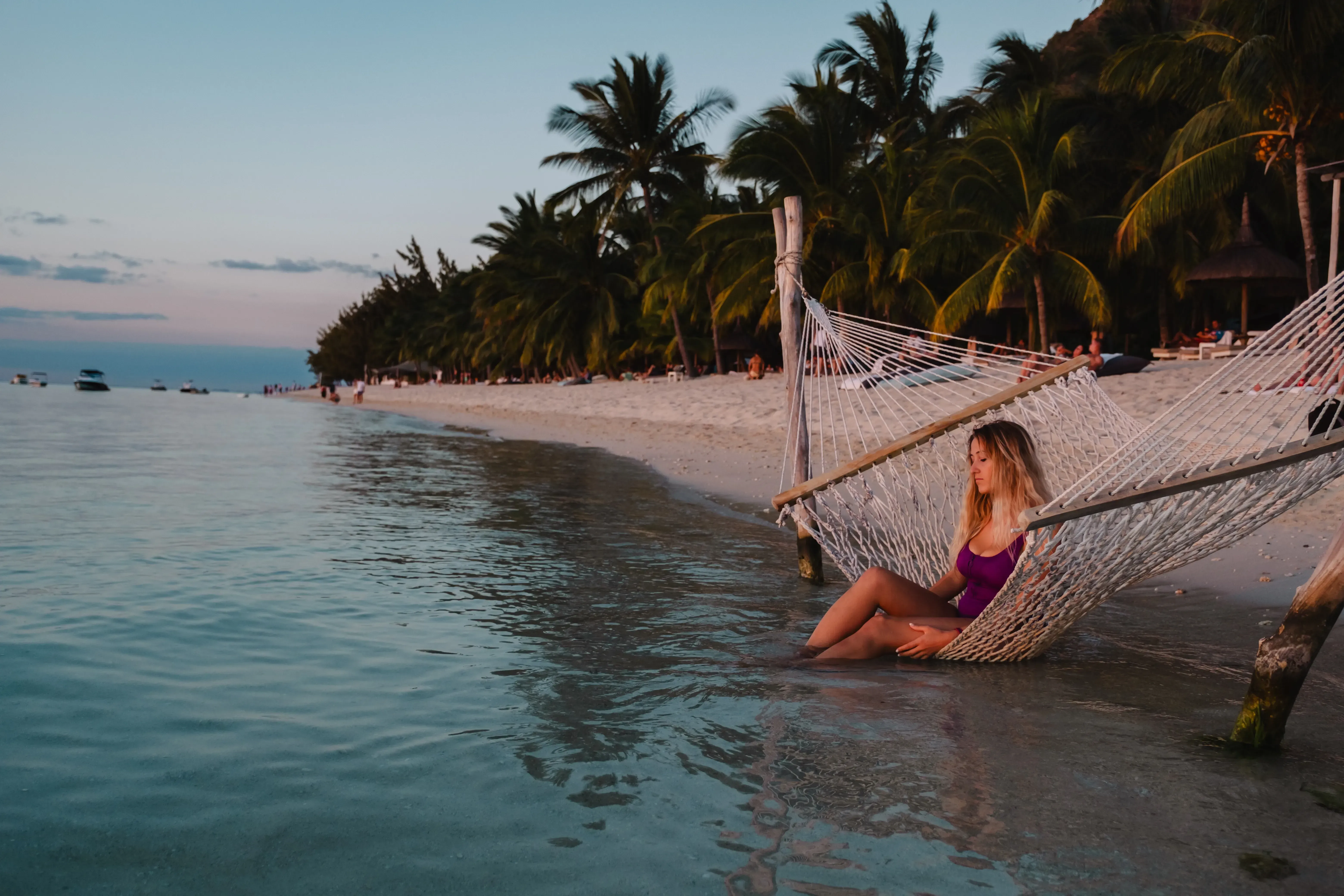 Letizia sitting or lying in a hammock suspended between palm trees on Le Morne beach.