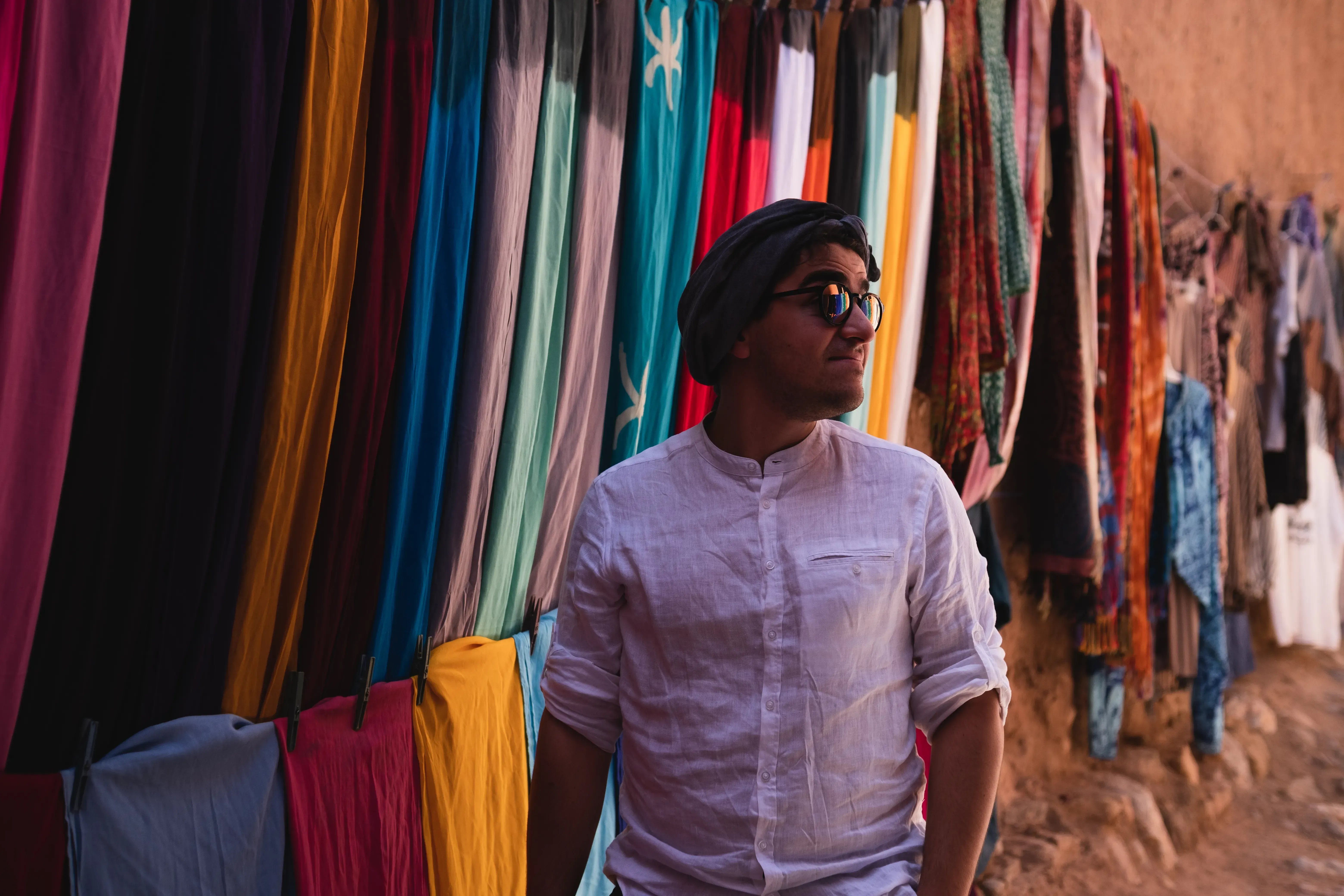 Person standing in front of a display of brightly colored Moroccan textiles and fabrics.