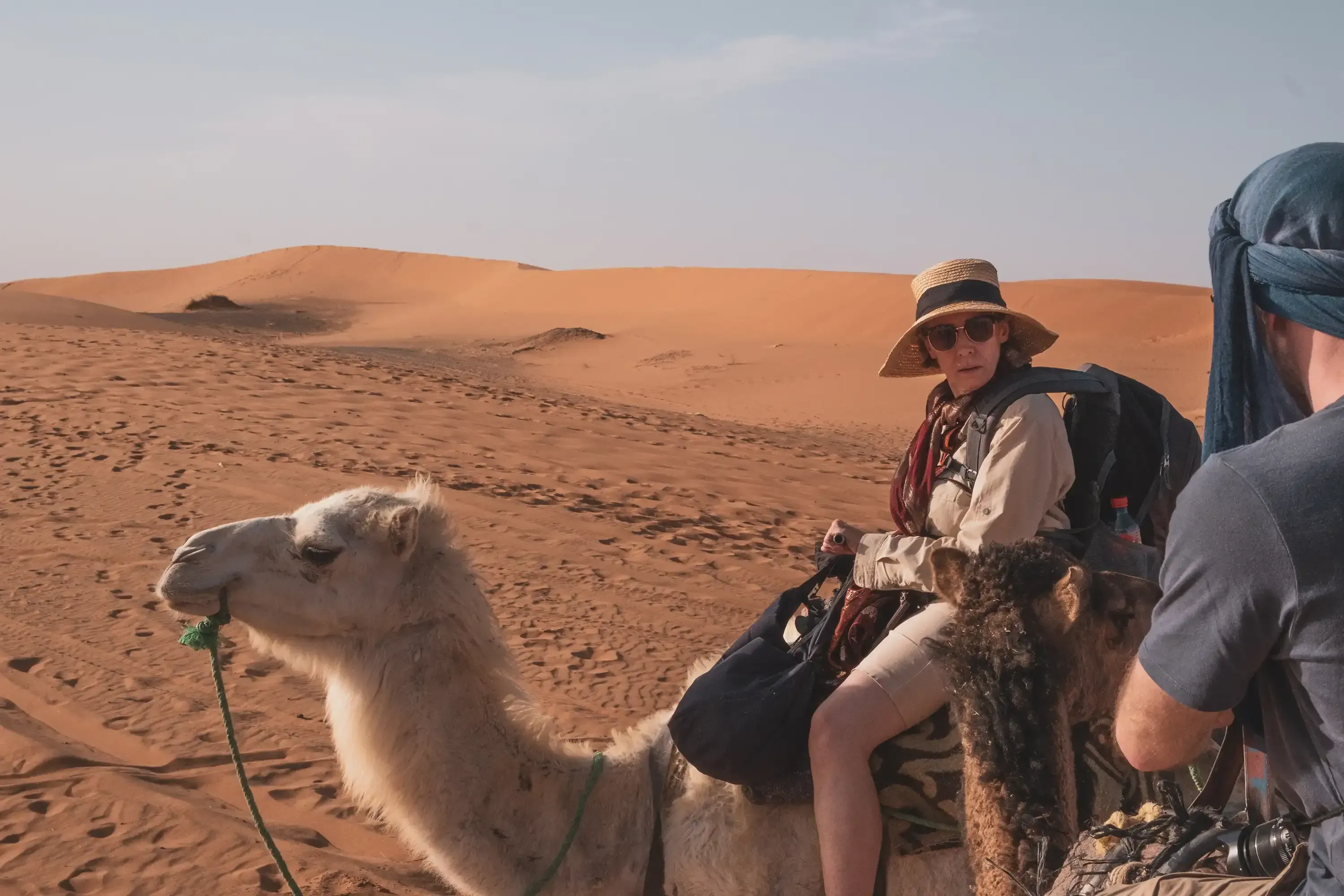 Close-up insert photo showing a woman riding a dromedary camel through the desert.