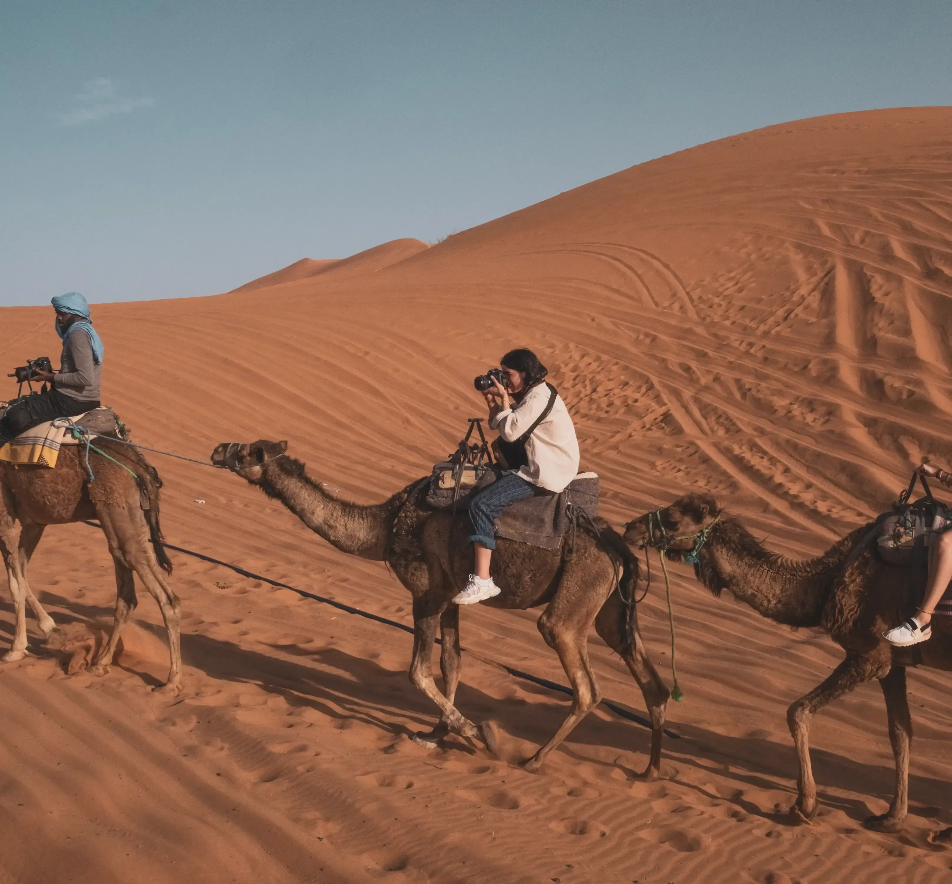 A girl taking a picture of the desert while riding a dromedary camel.