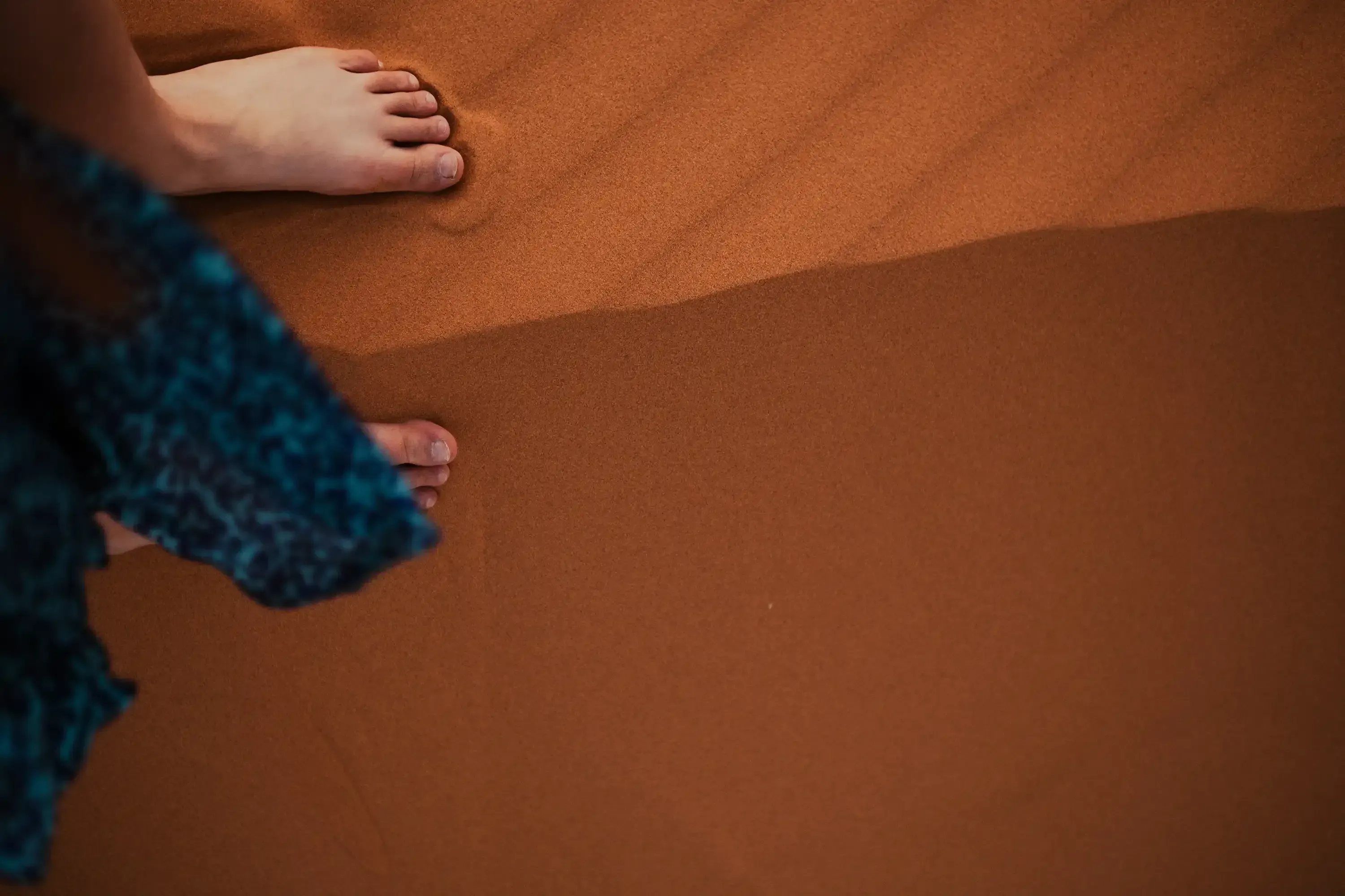 Close-up of bare feet sinking slightly into the warm desert sand.