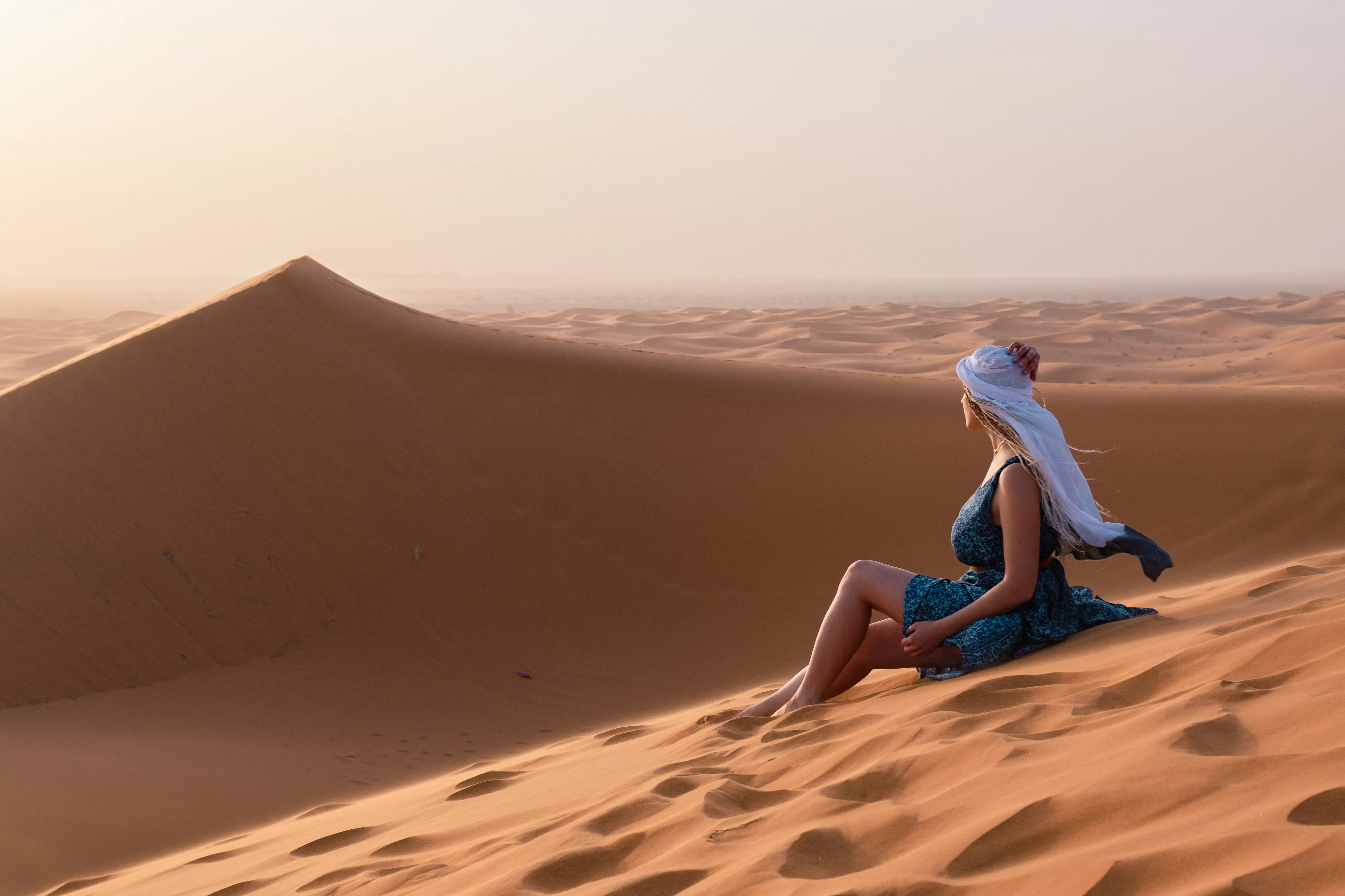 Letizia sitting down on the crest of a large, soft sand dune.