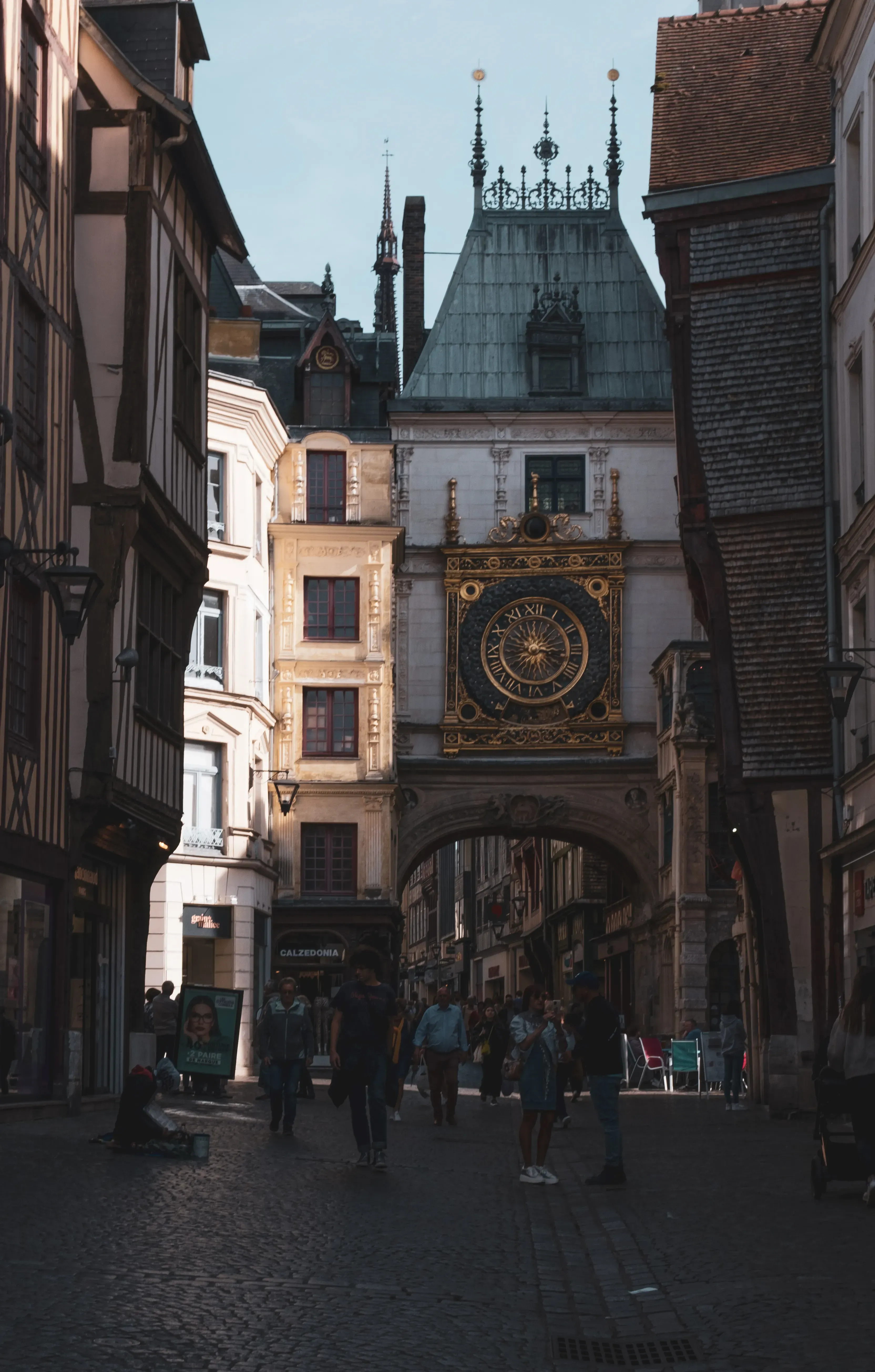 The ornate, golden clock or timepiece, likely referencing the Gros Horloge in Rouen.