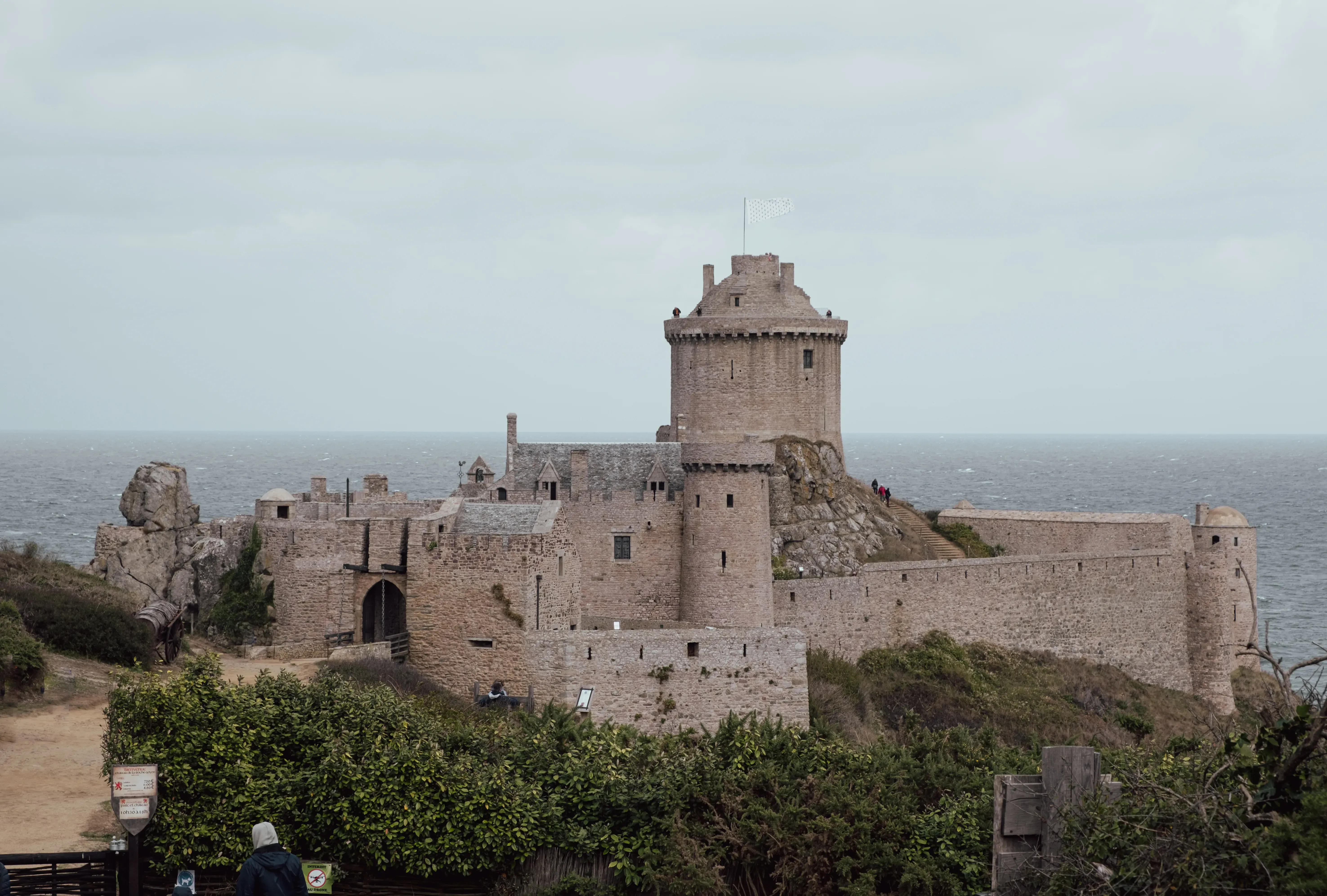 A distant view of the medieval Fort La Latte castle positioned dramatically on the rocky coastline.