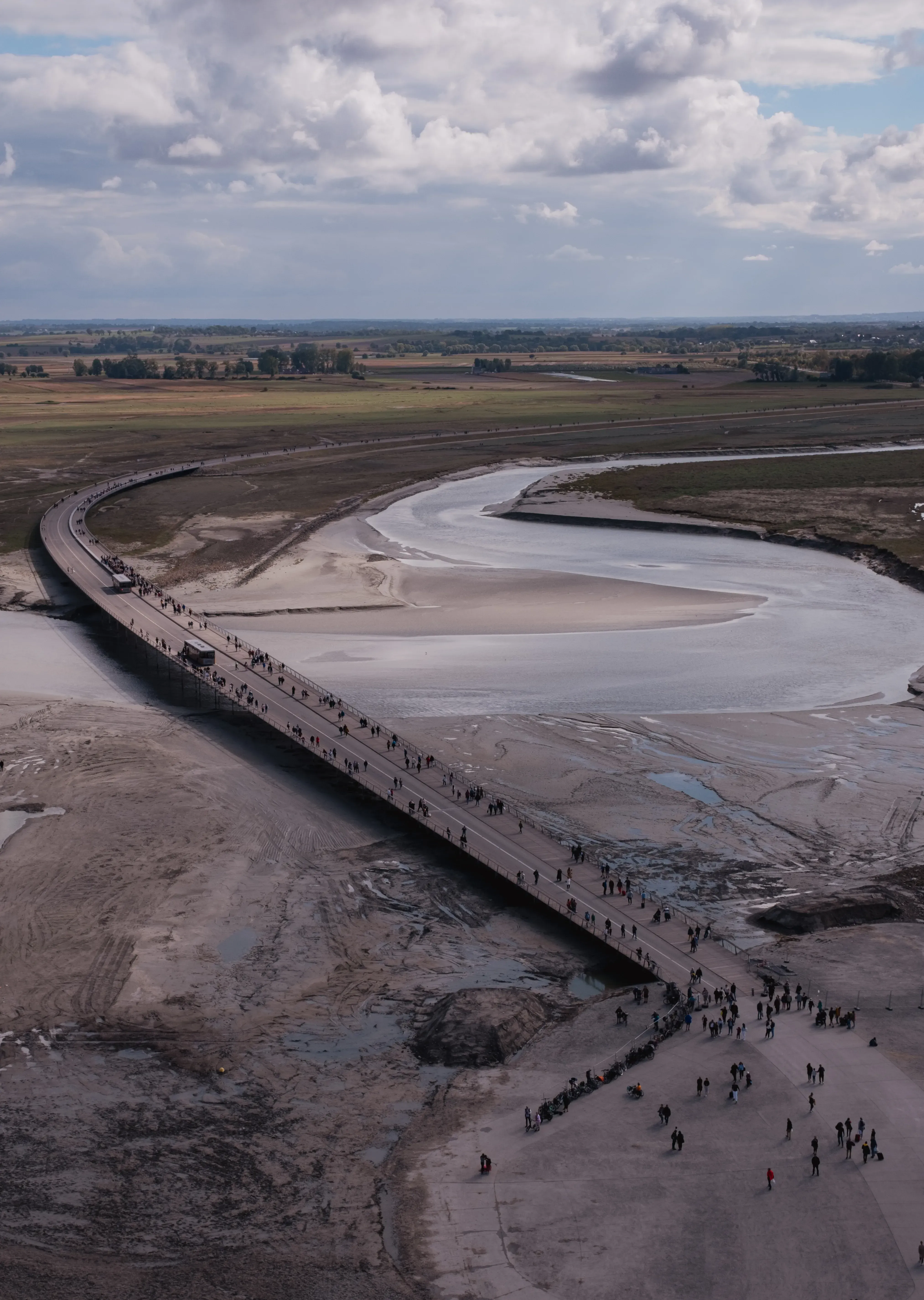 An aerial or high-vantage view showing the causeway or bridge leading across the sand to Mont Saint-Michel island.