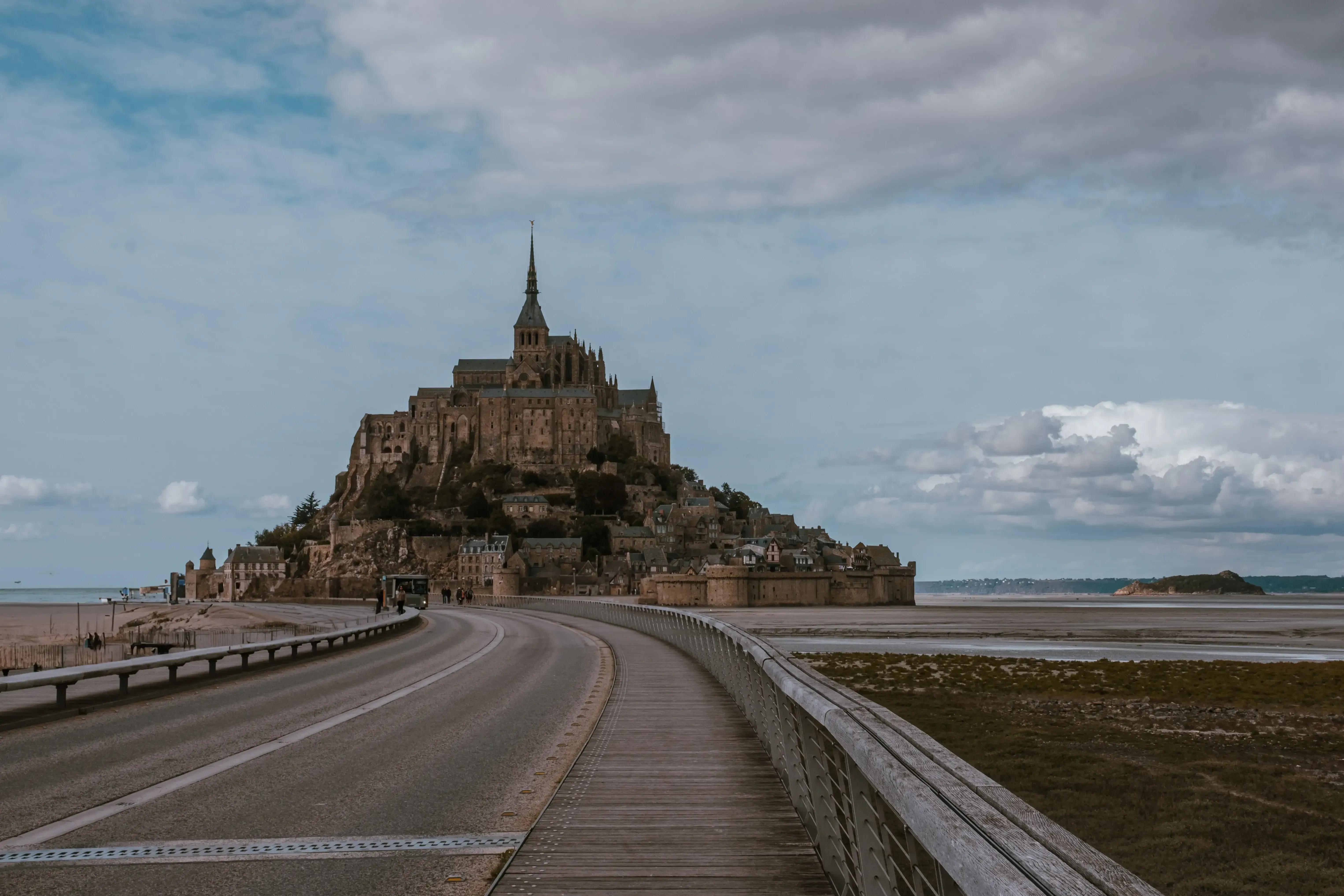 The tidal island Mont Saint-Michel seen from a distance, showing the causeway or bridge connecting it to the mainland.