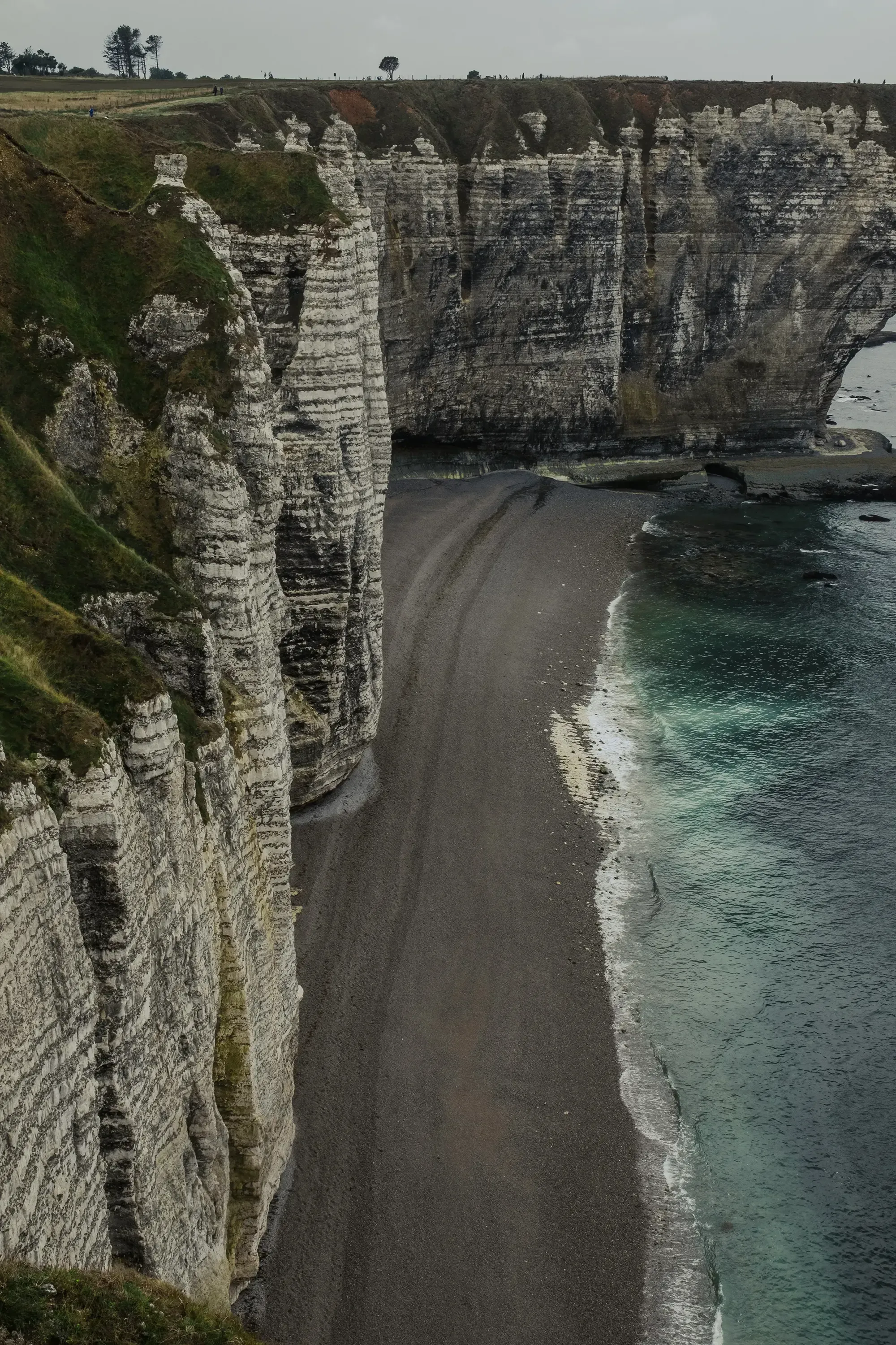 A lush green field (plateau) ending abruptly at the dramatic white limestone cliff edge of Étretat.