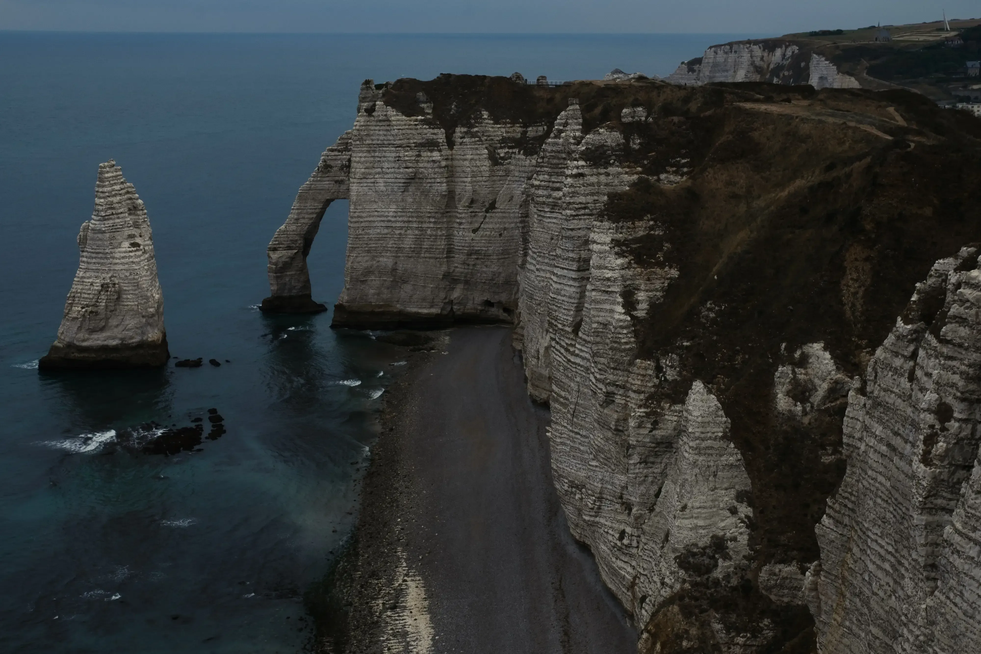 A bird's-eye view of the crescent-shaped pebble beach of Étretat and the town waterfront.
