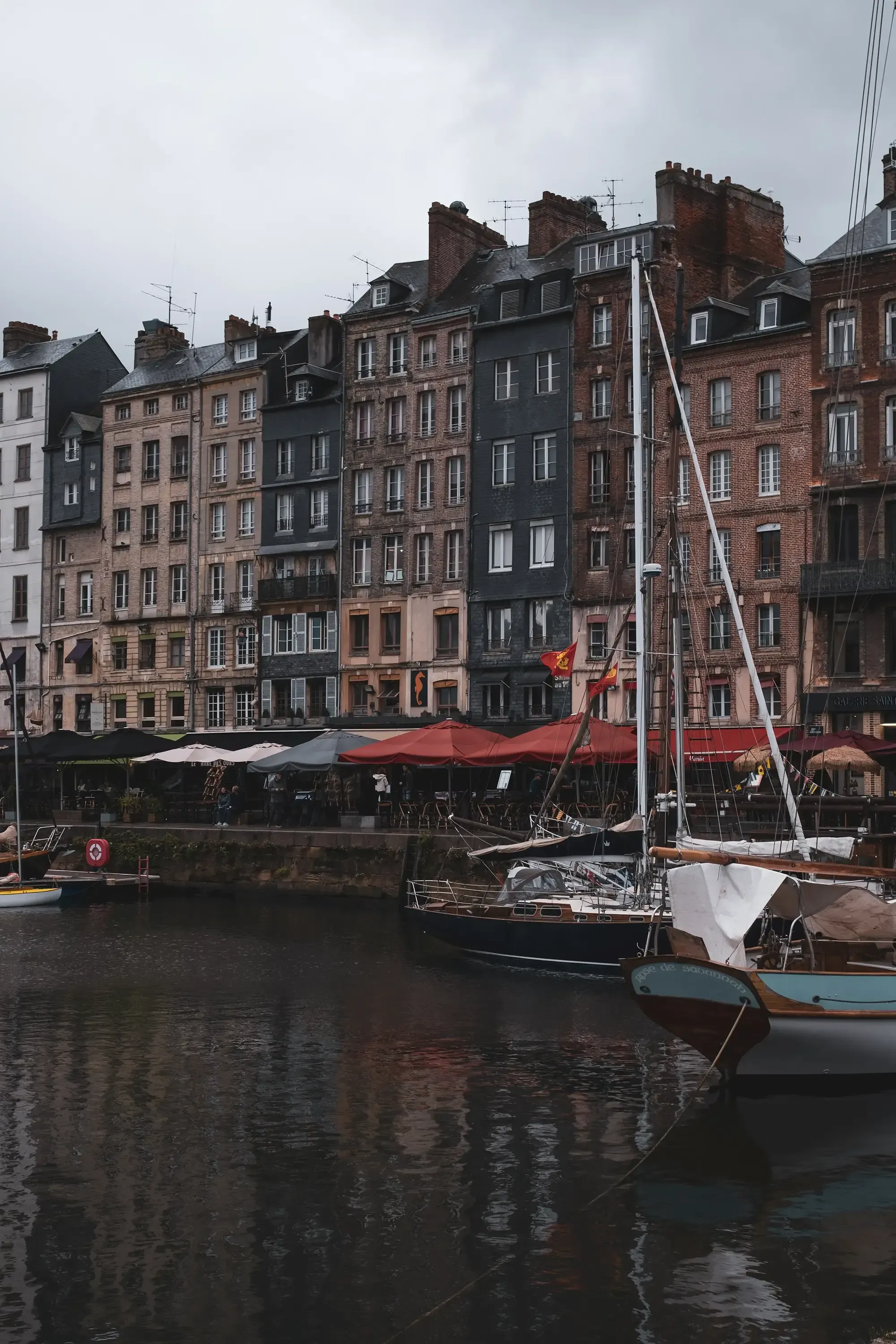 Colorful boats and yachts moored in the main dock (molo) area of Honfleur harbor.