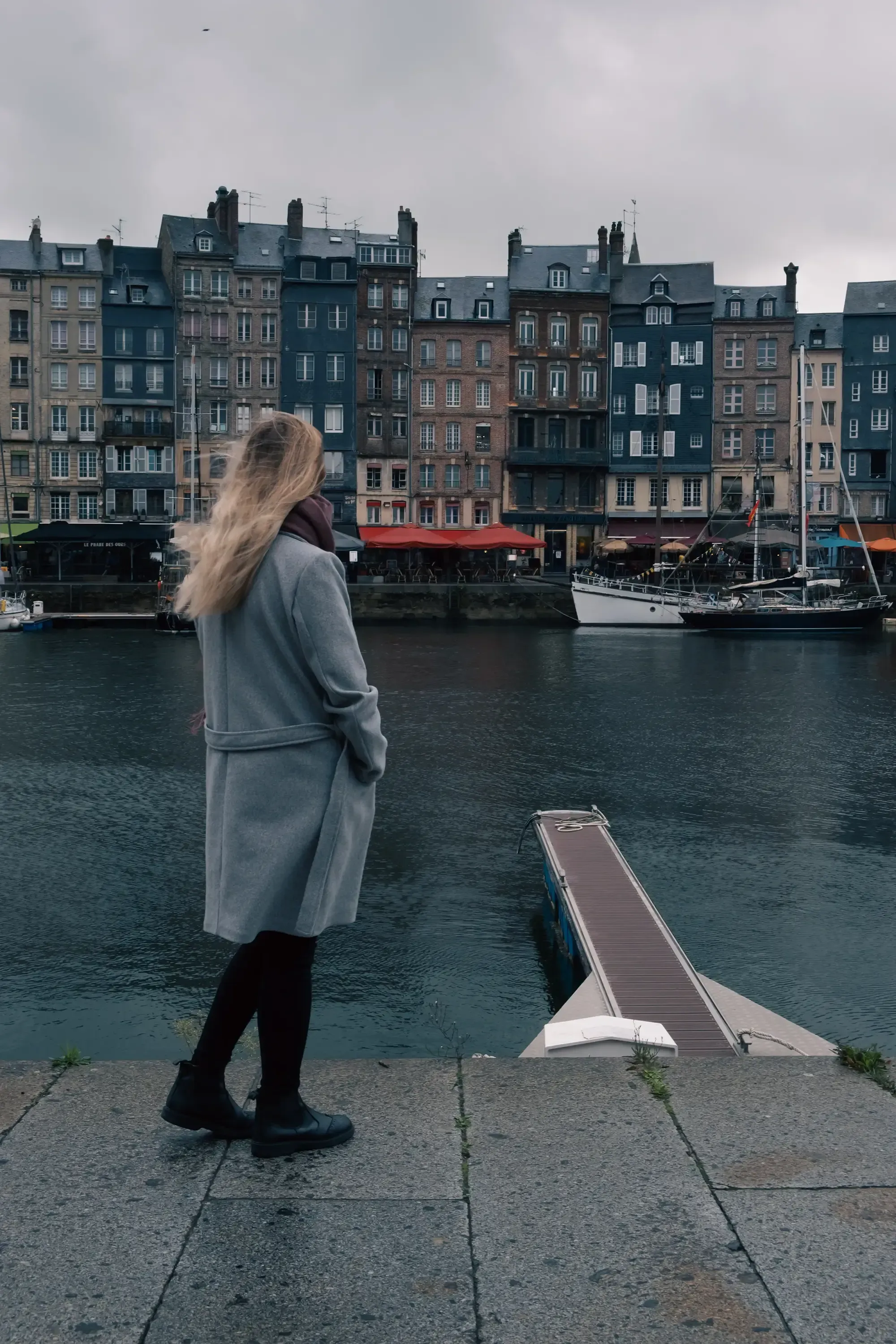 Letizia standing in the street or near the historic houses bordering the harbor in Honfleur.