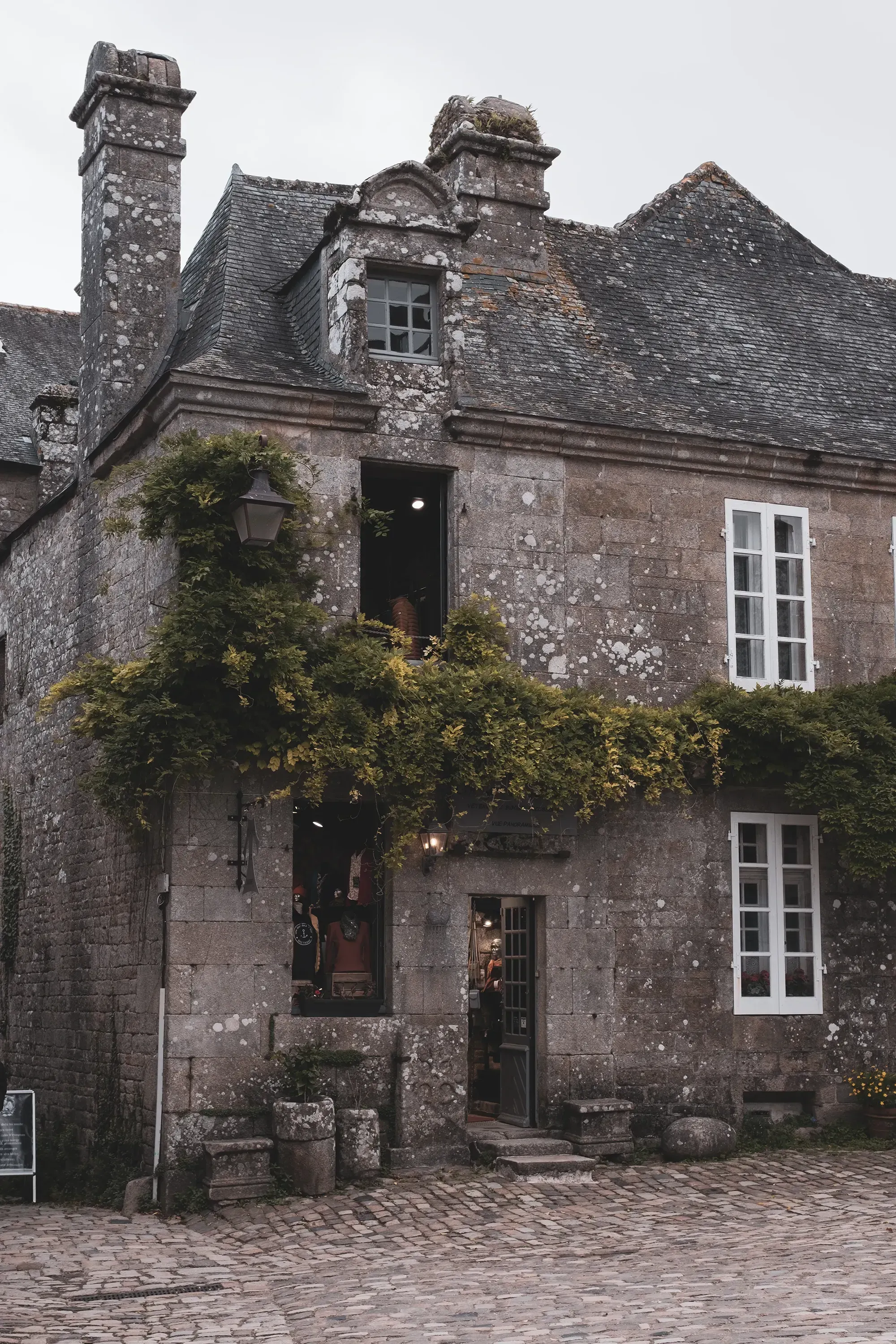A view of a historic granite house along a cobblestone street in the medieval town of Locronan, Brittany.