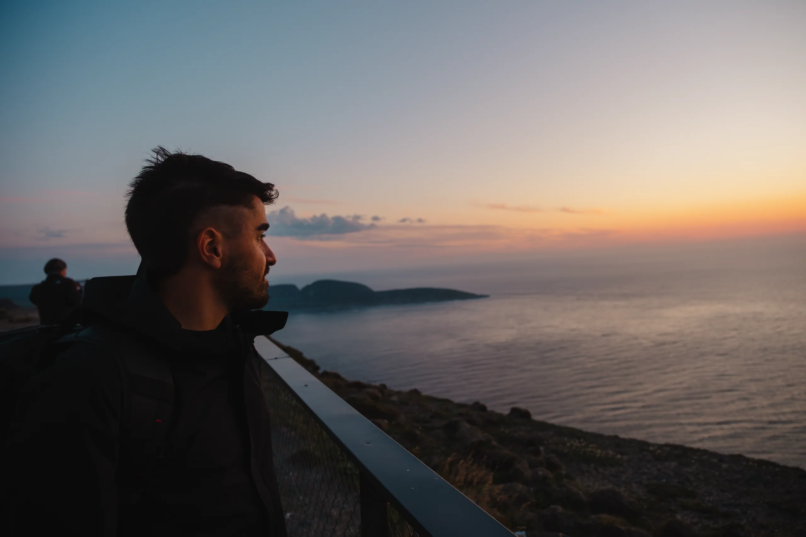 Person standing at North Cape, gazing at the sea under the Arctic Midnight Sun.