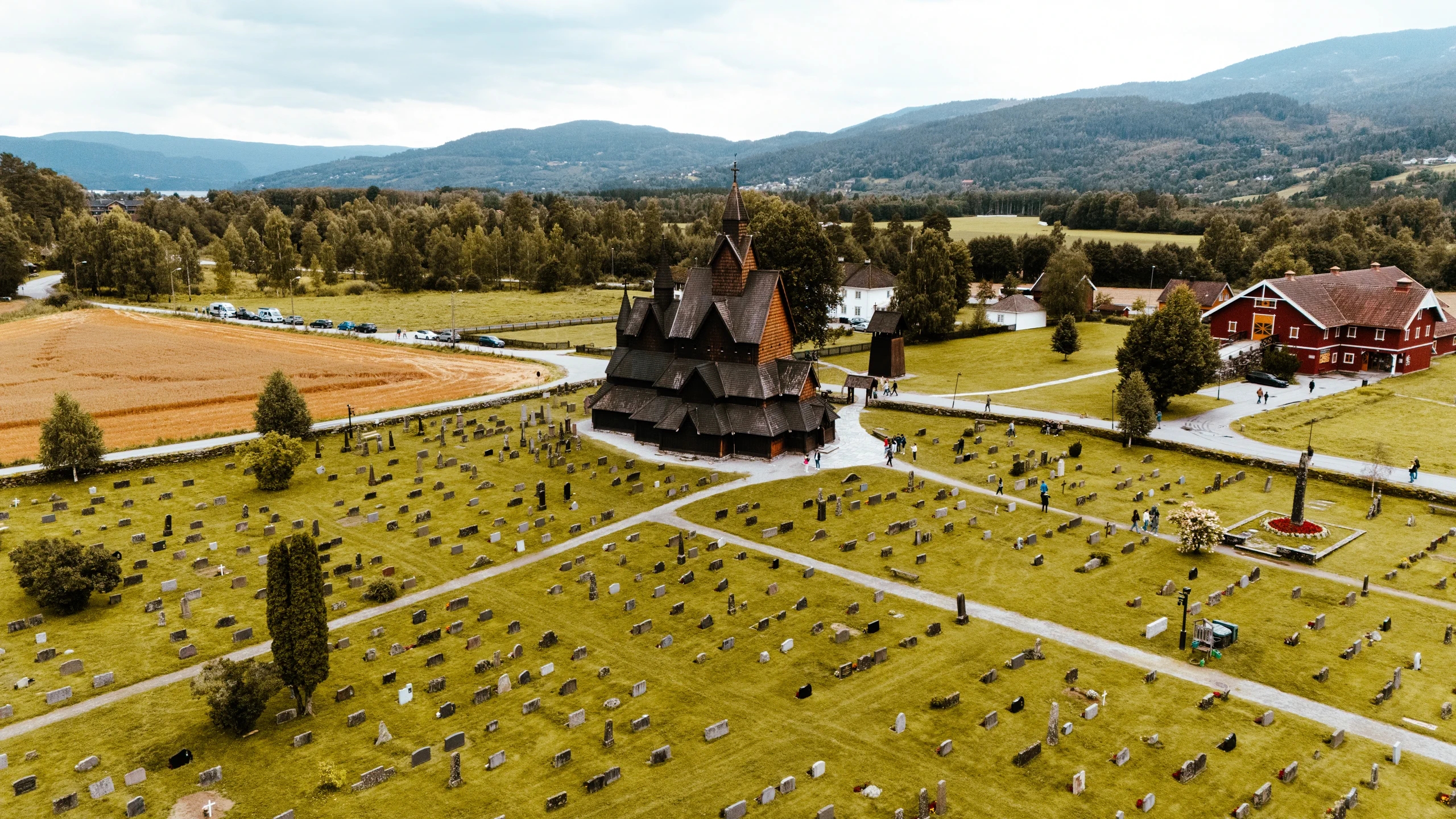 Traditional wooden Stave Church next to a small cemetery on a sunny, bright green day in Norway.