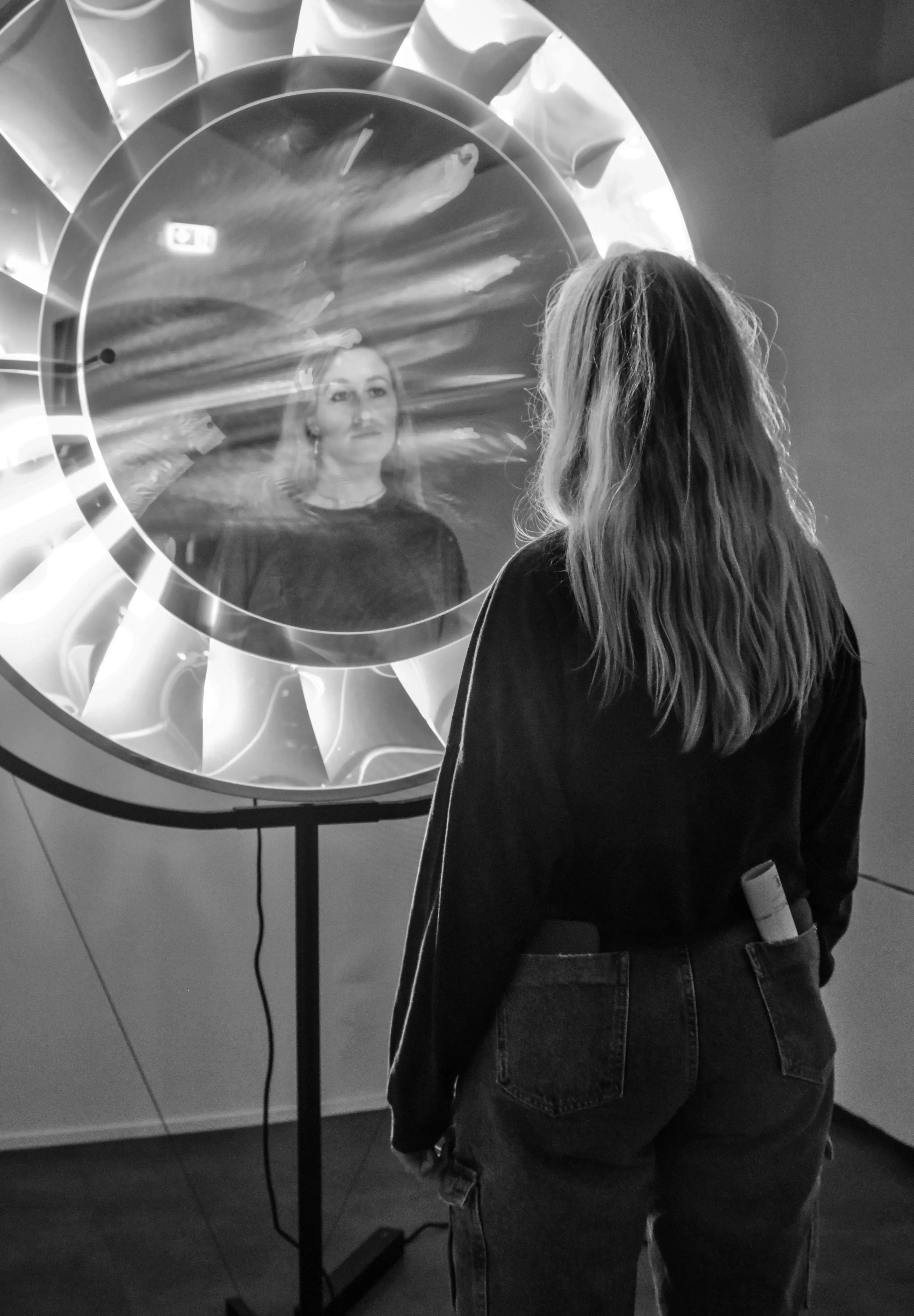 Letizia looking at her reflection in a large, mirrored surface within the exhibit.