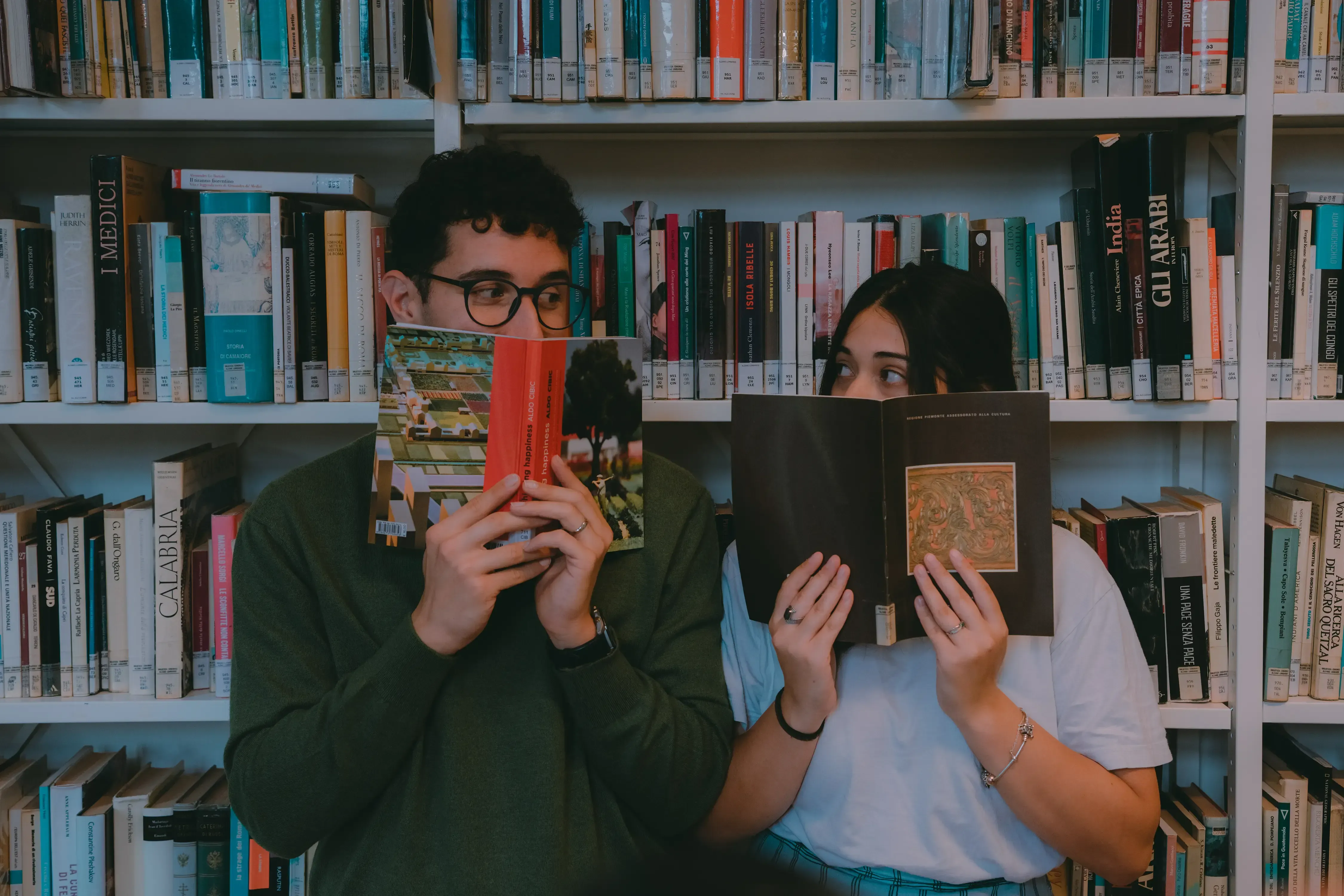 Paolo and Paulina looking and peeking at each other from behind large books.