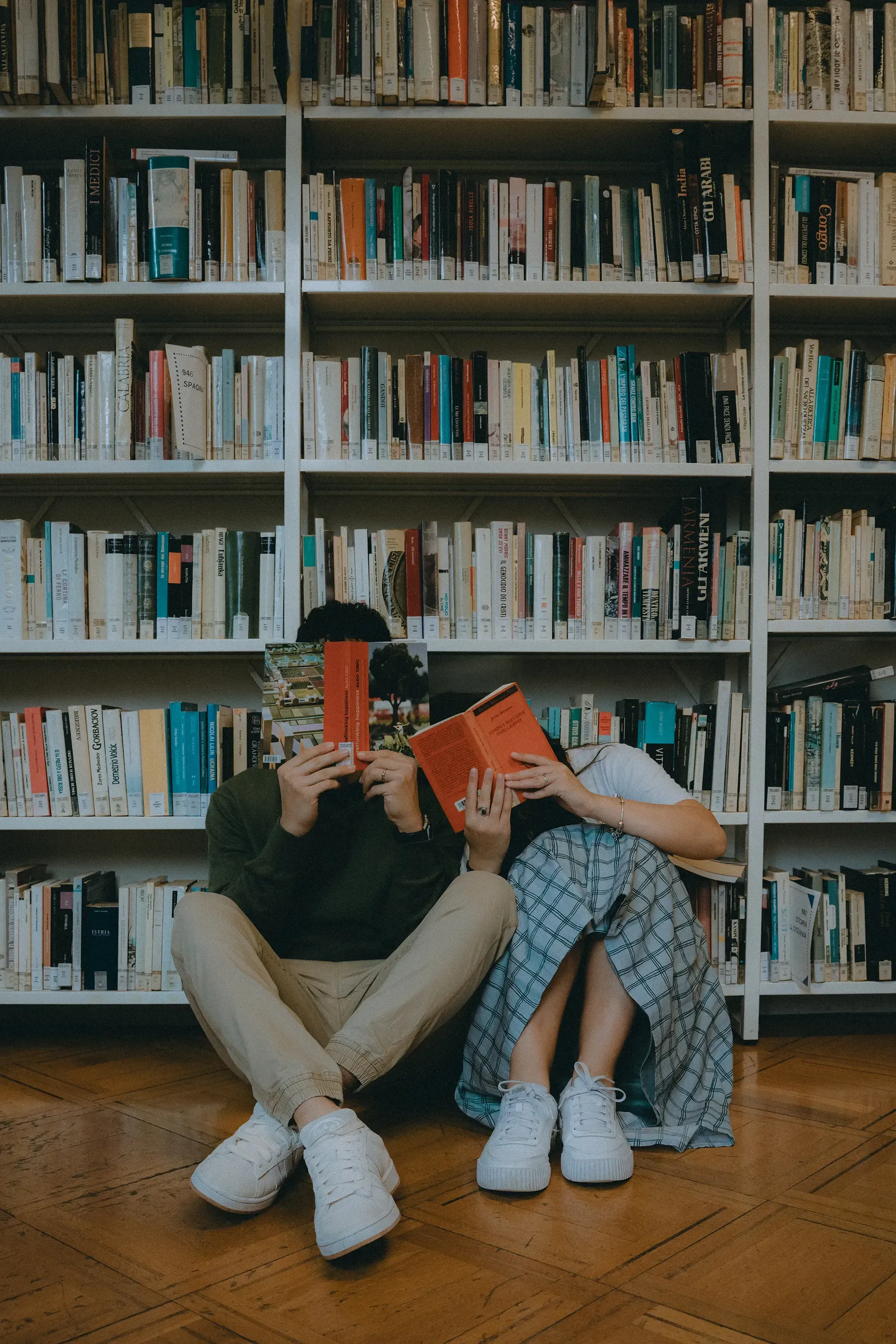 Paolo and Paulina sitting in the library aisle, faces hidden by the books they are reading.