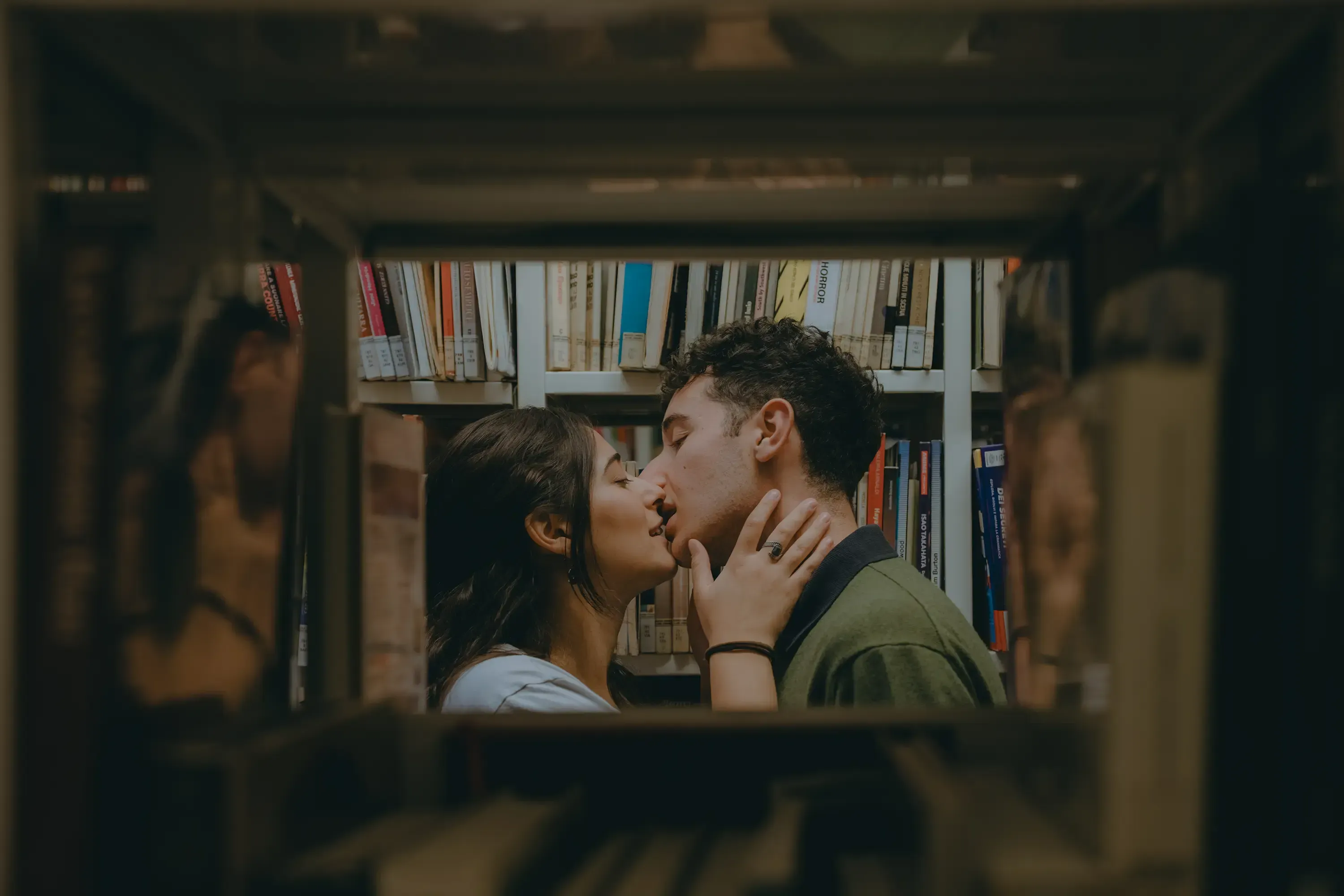 Paolo and Paulina kissing, framed by the towering bookshelves in the library background.