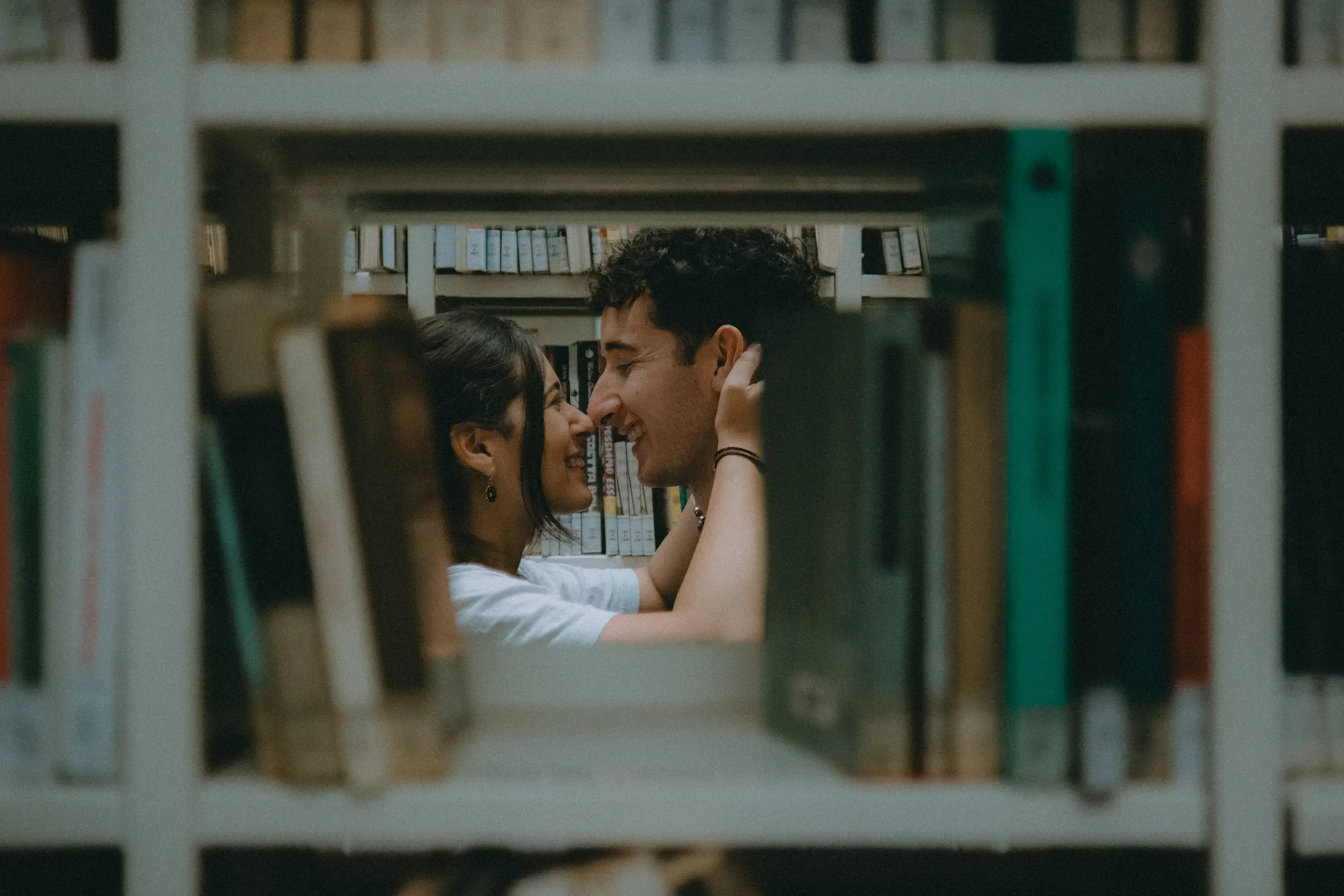 Paolo and Paulina bringing their heads close together, framed by library book spines.