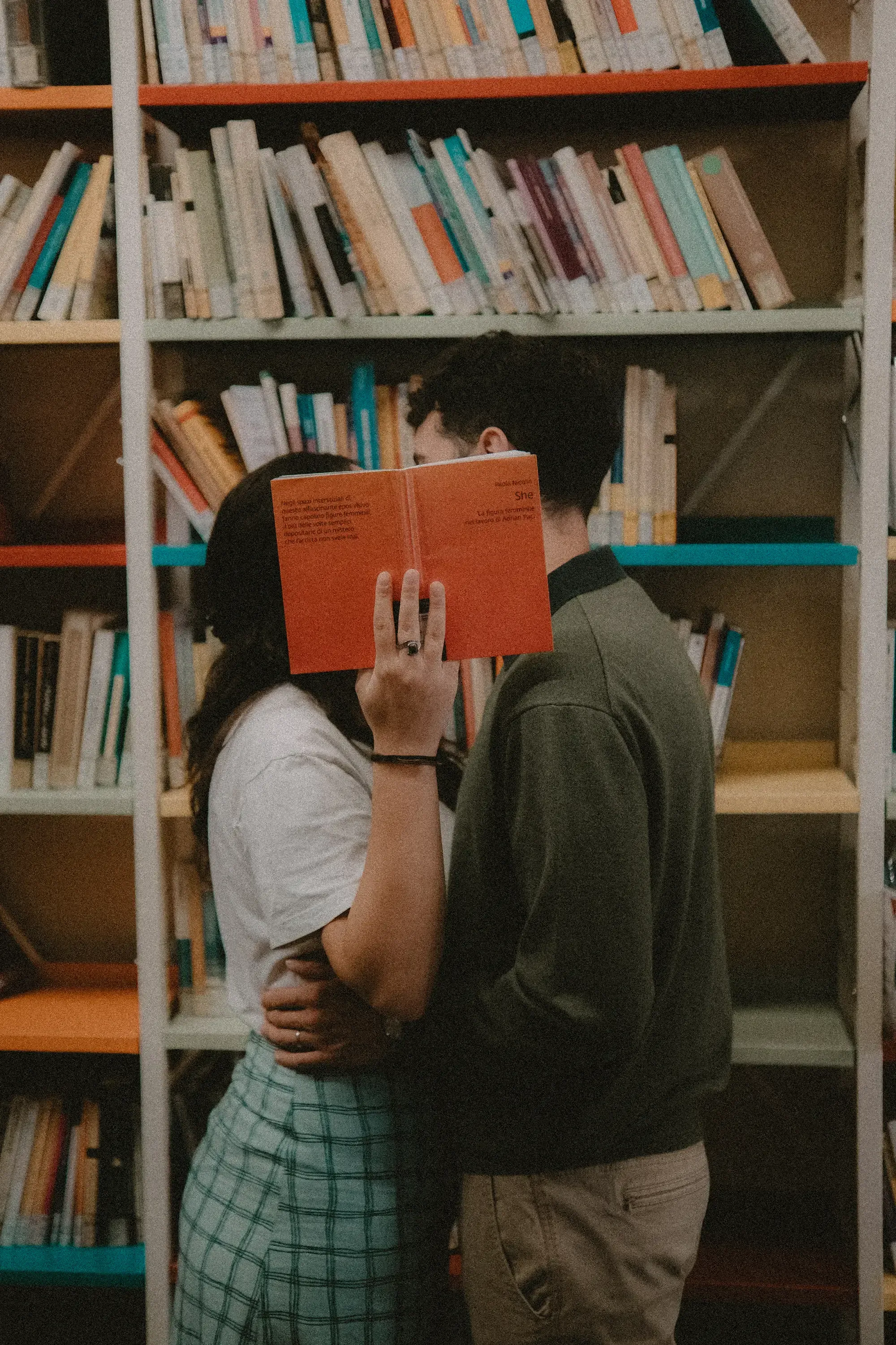 Paolo and Paulina kissing behind two books they hold up to conceal their faces.