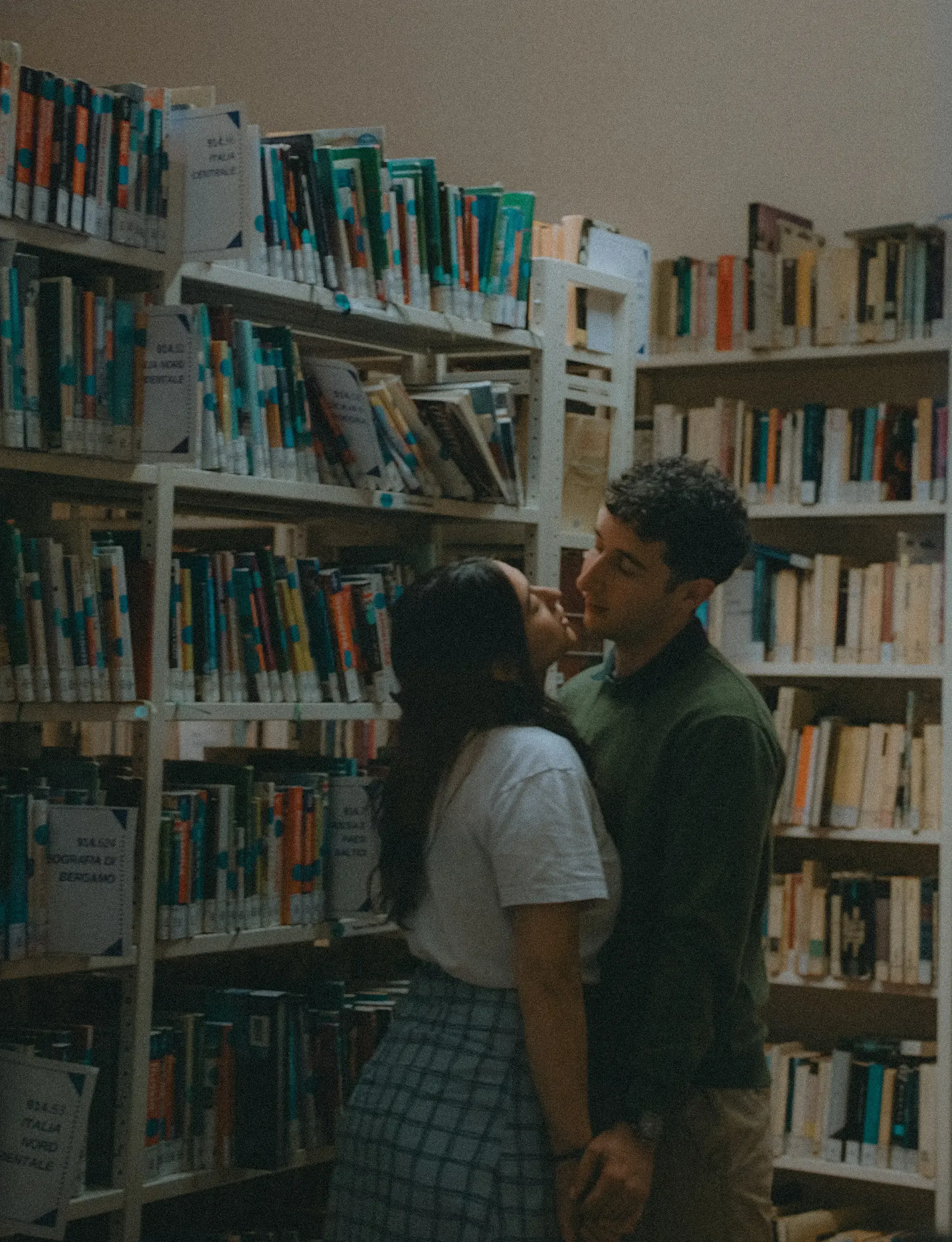 Paolo and Paulina holding hands while kissing in a library.