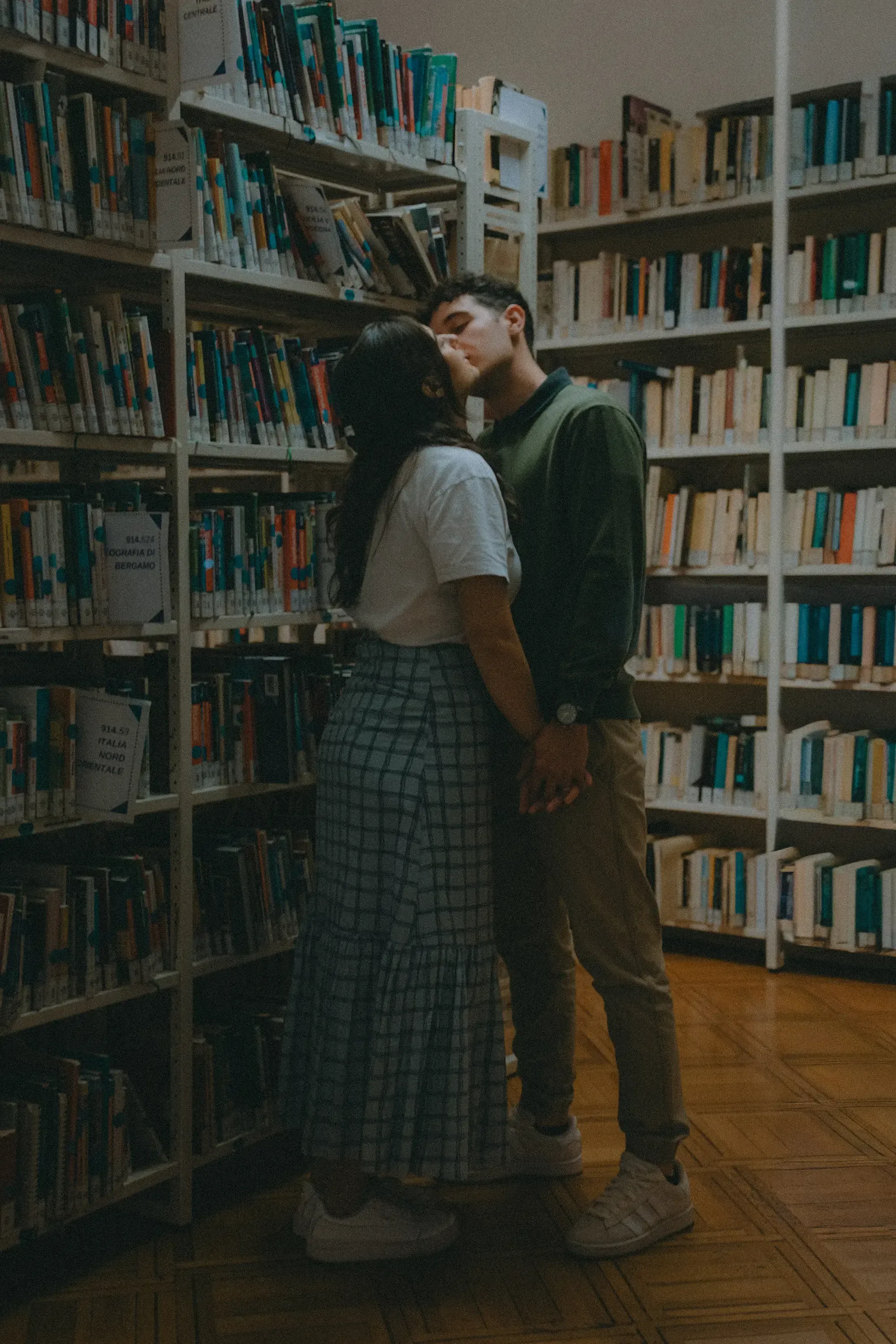 Paolo and Paulina sharing a kiss between the packed library book stacks.