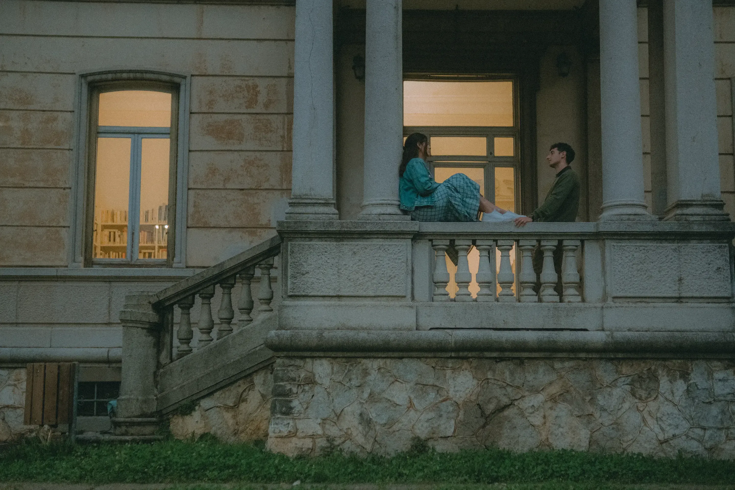 Paolo looking at Paulina, who is sitting on a small wall outside the library building.