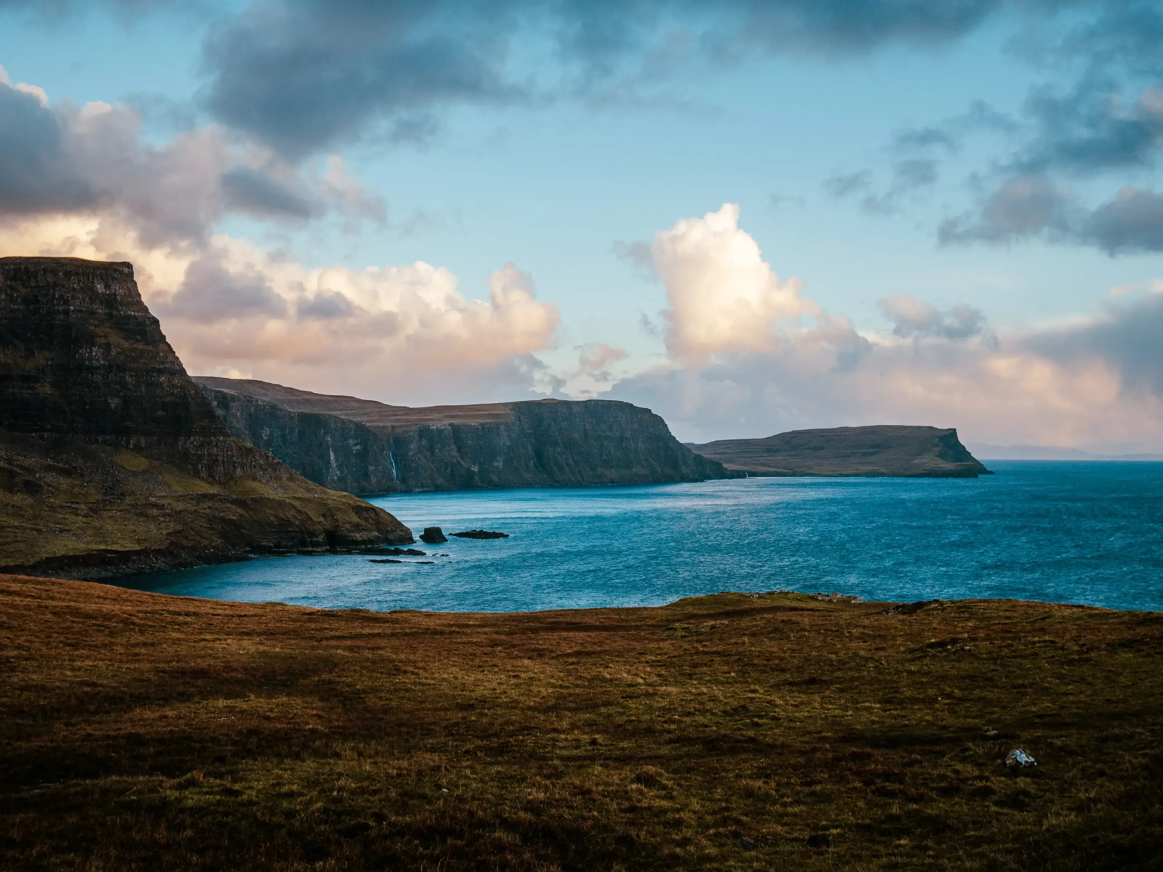 The rough, dark waters of the sea crashing against the towering stone cliffs of the Scottish coast.
