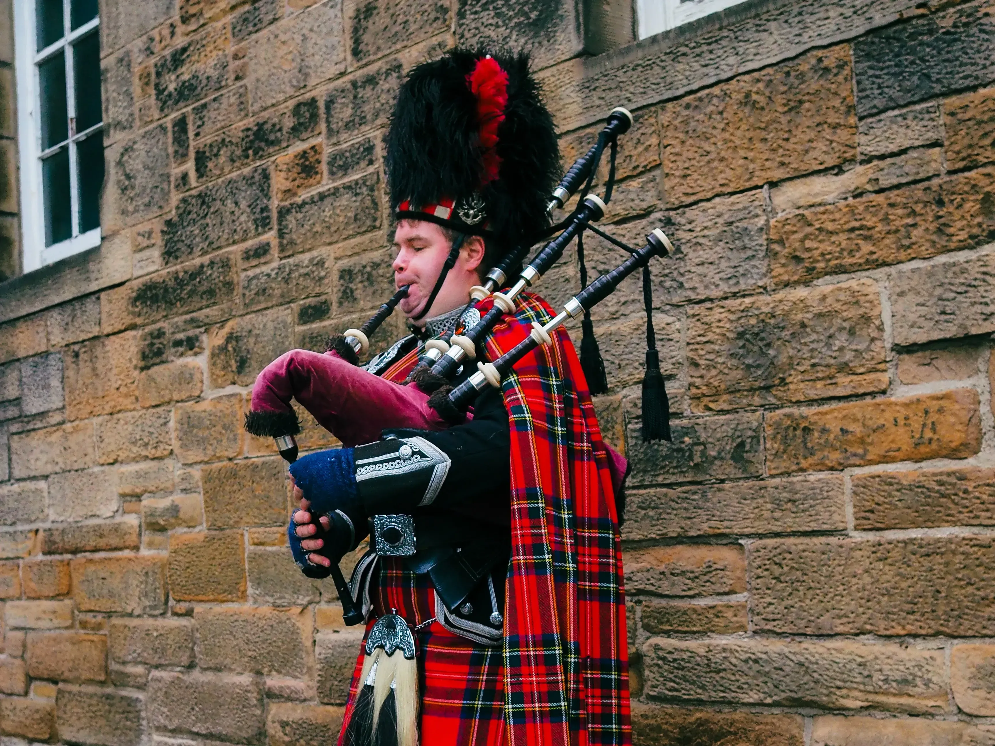 Street performer dressed in kilt playing the traditional bagpipes in Edinburgh.