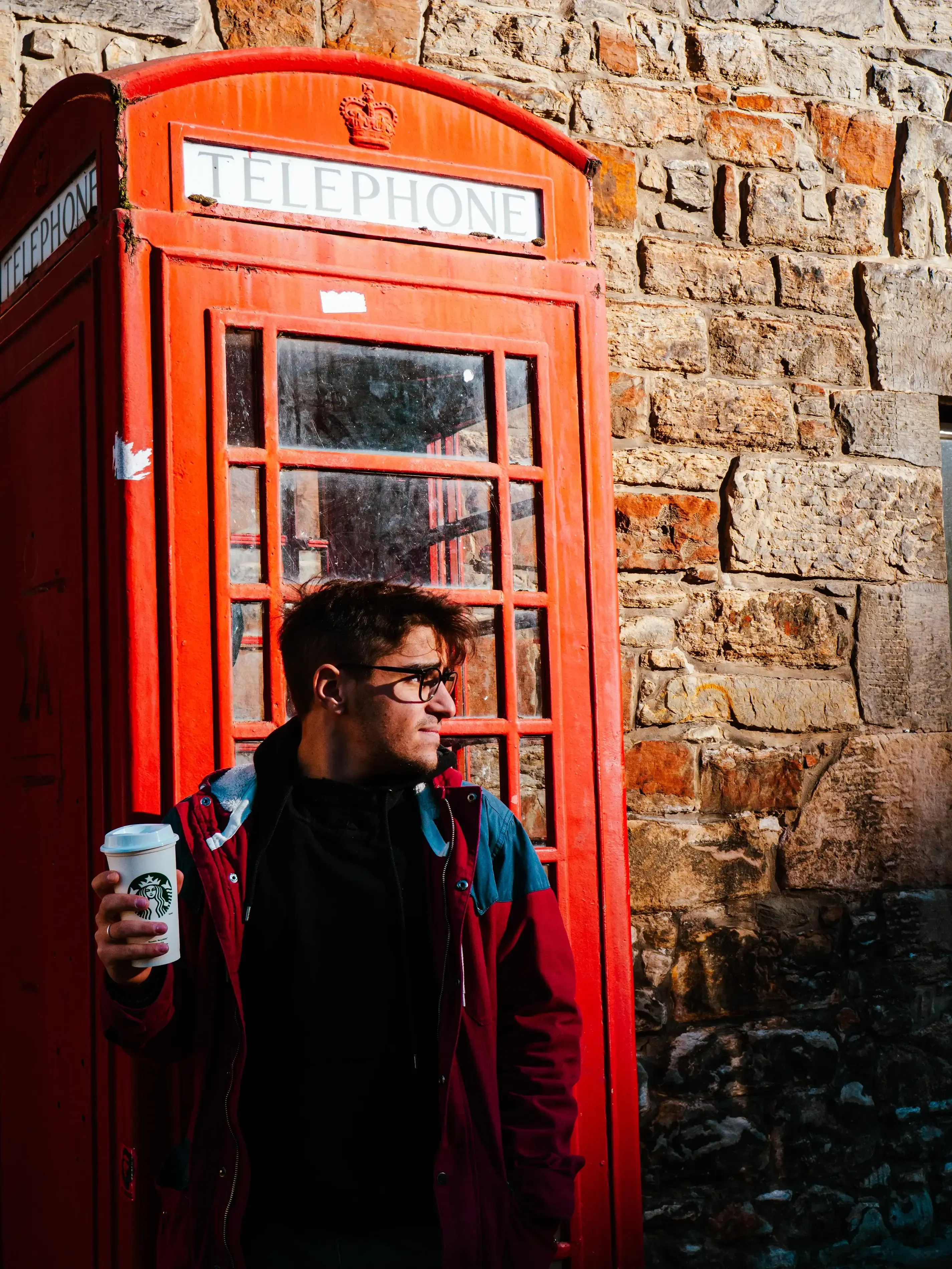 Person standing next to a classic red British telephone box.