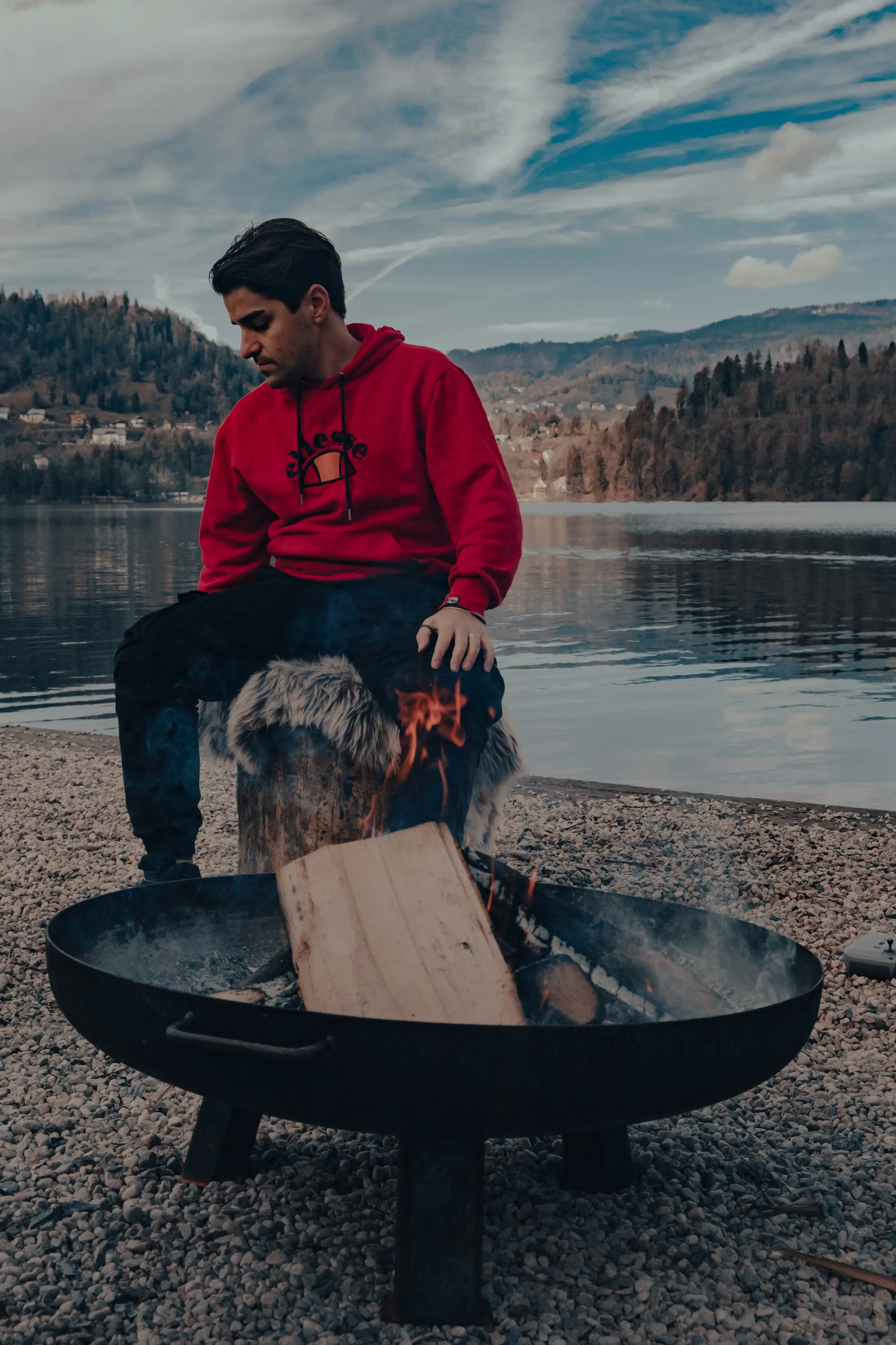 Ieser sitting comfortably near a small campfire or bonfire on the shore of Lake Bled.