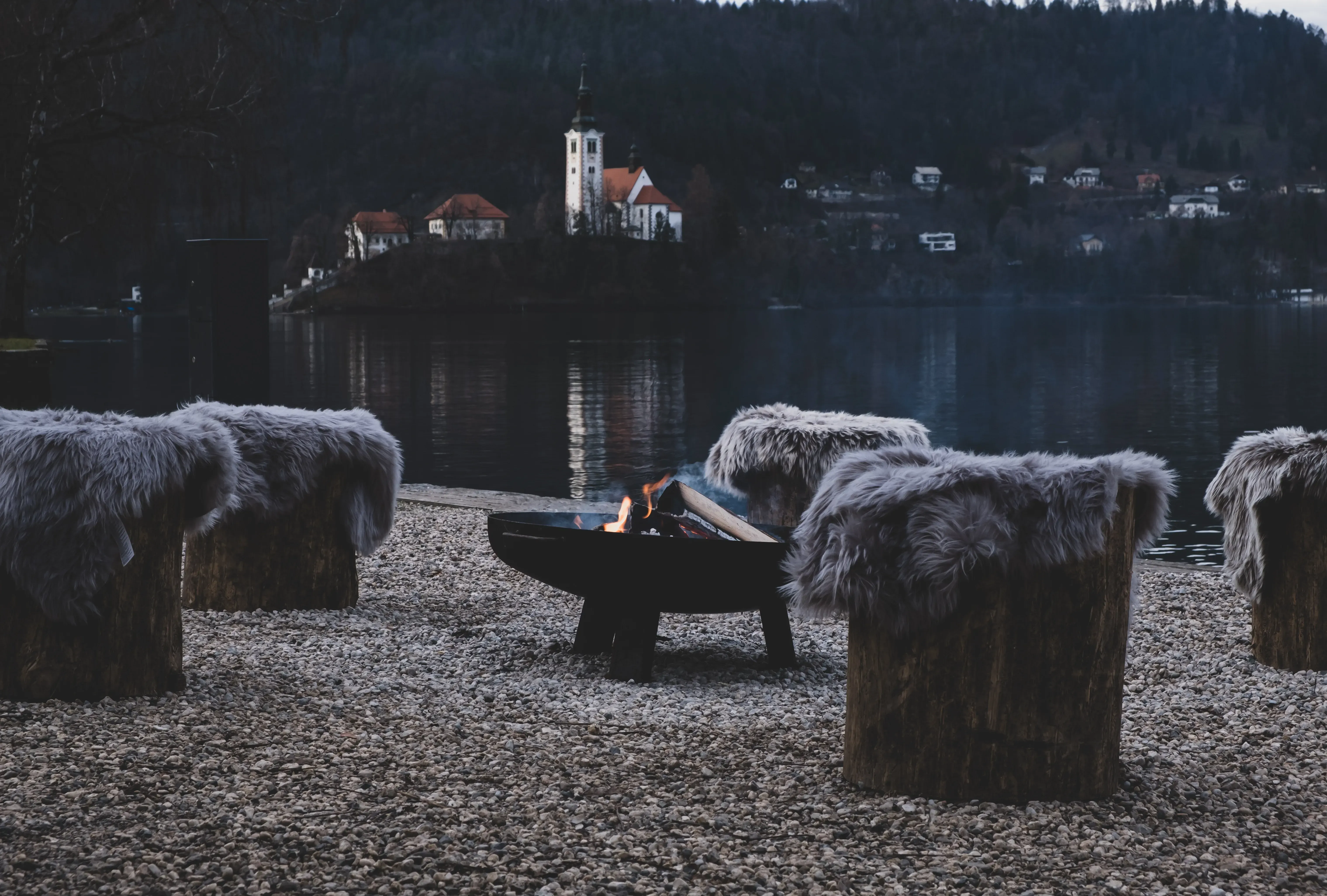 An outdoor bar area near Lake Bled with a central bonfire (falò) providing warmth and ambiance.