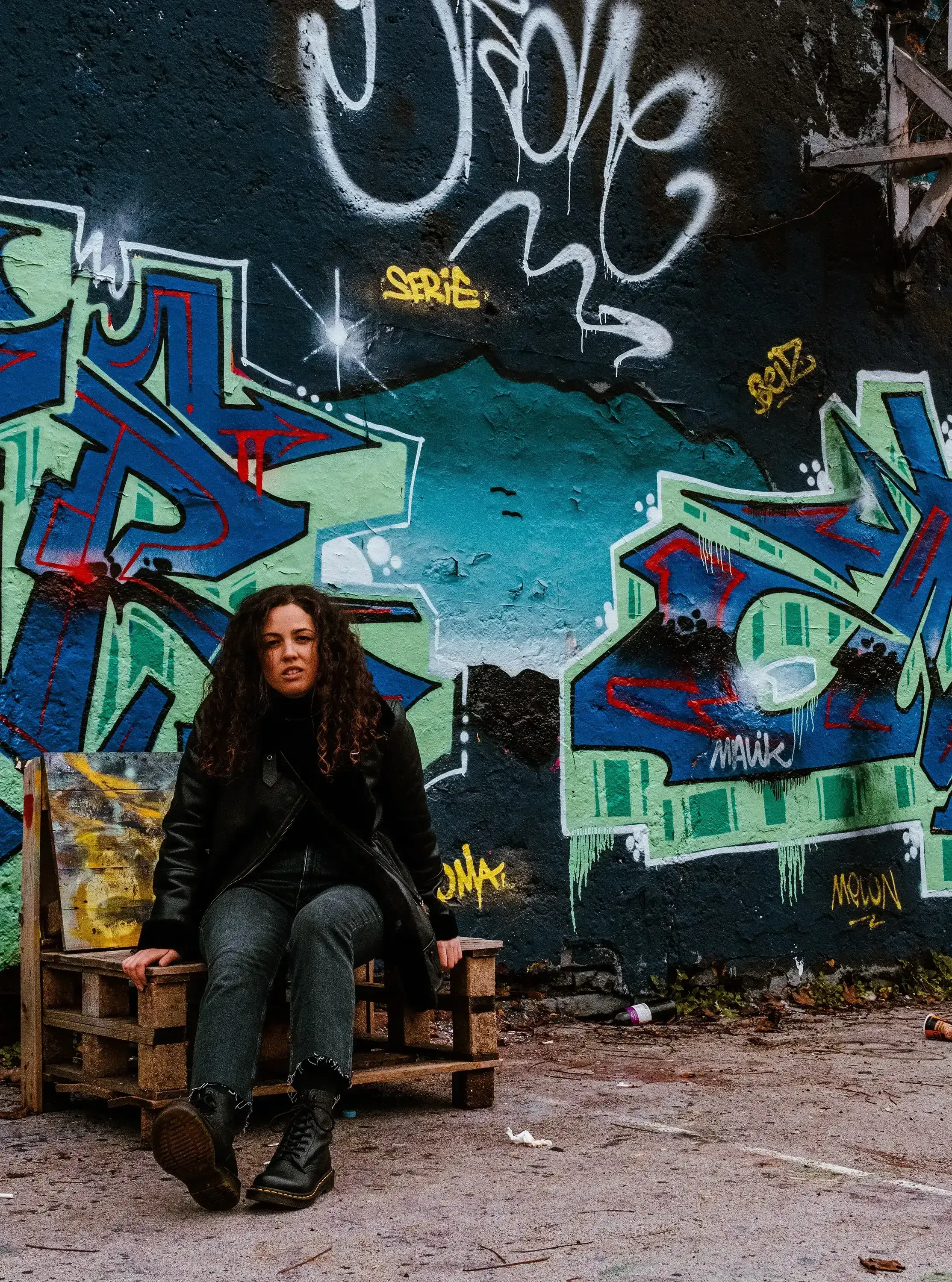 Beatrice sitting on a stack of wooden pallets in a setting within the town of Metelkova.