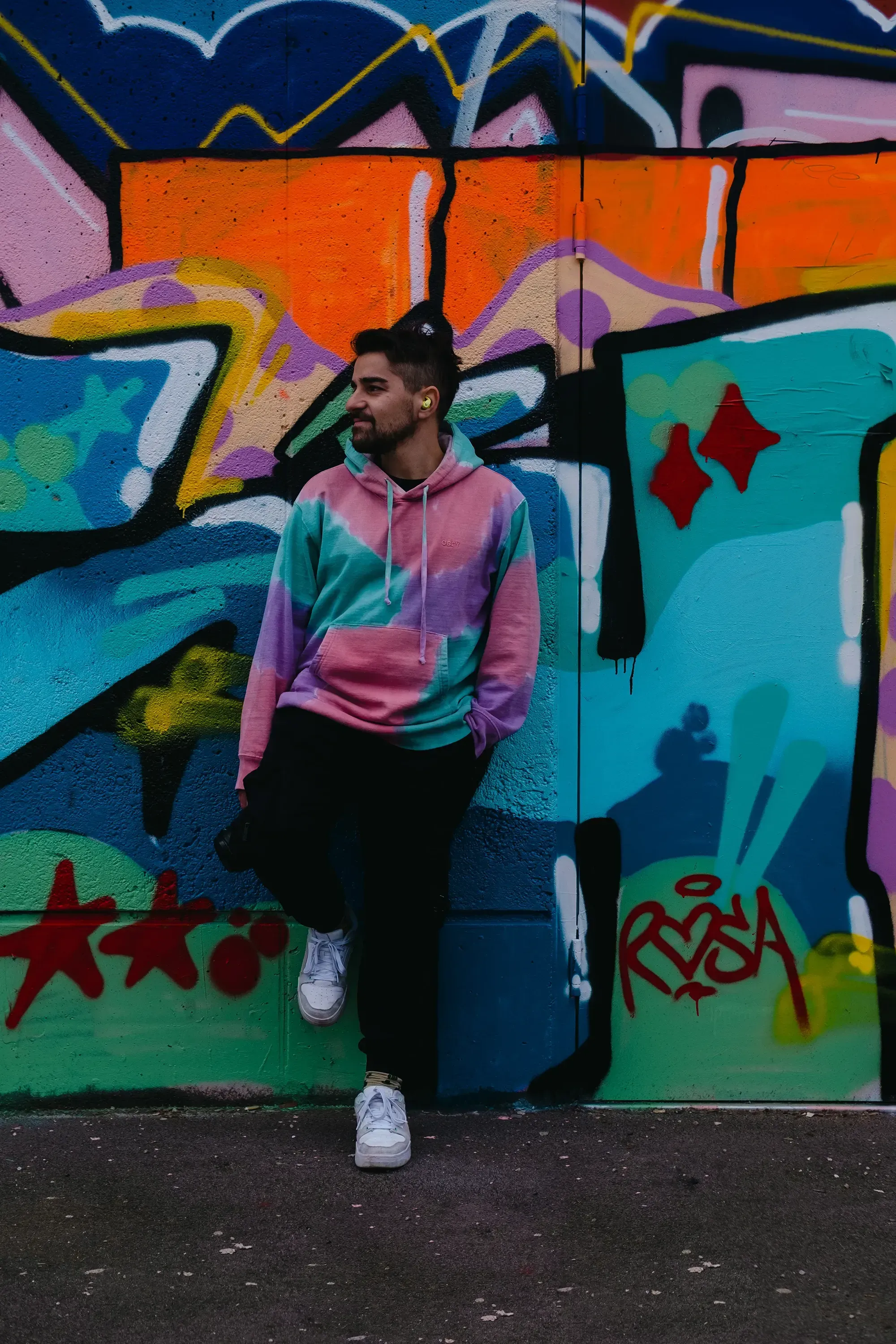 Ieser leaning against a wall covered in street art graffiti.